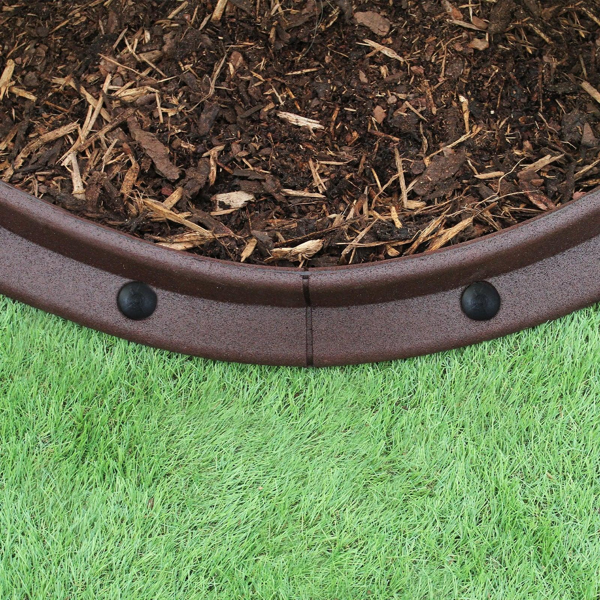 Flexible brown lawn edging in a curved shape, made from durable material, neatly borders mulch and green grass for a tidy garden look