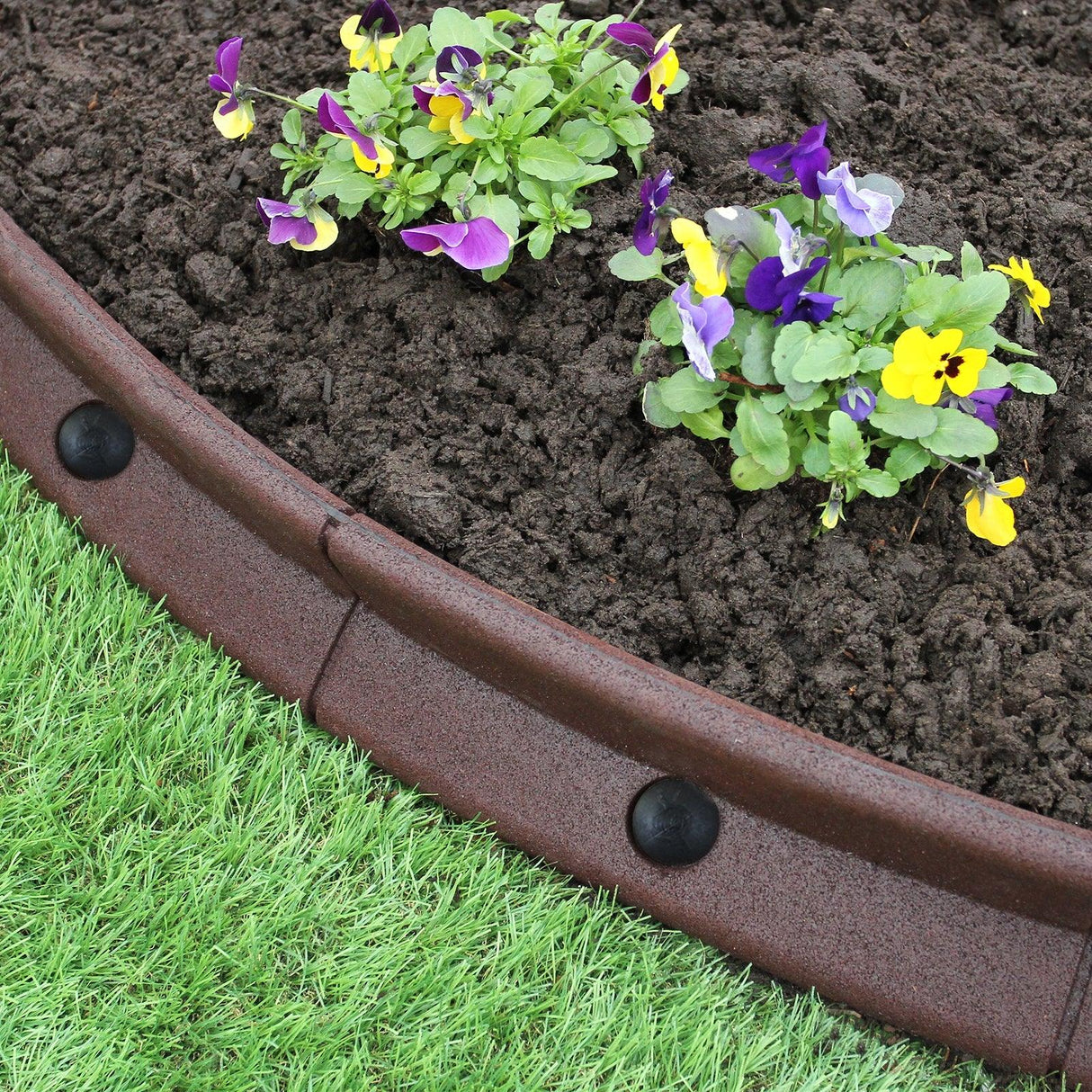 Flexible brown lawn edging with a smooth texture, surrounding vibrant purple and yellow flowers in rich dark soil