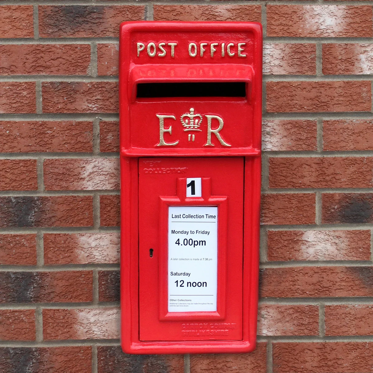 Bright red Royal Mail post box mounted on a brick wall, featuring a crown emblem, collection times, and a classic design