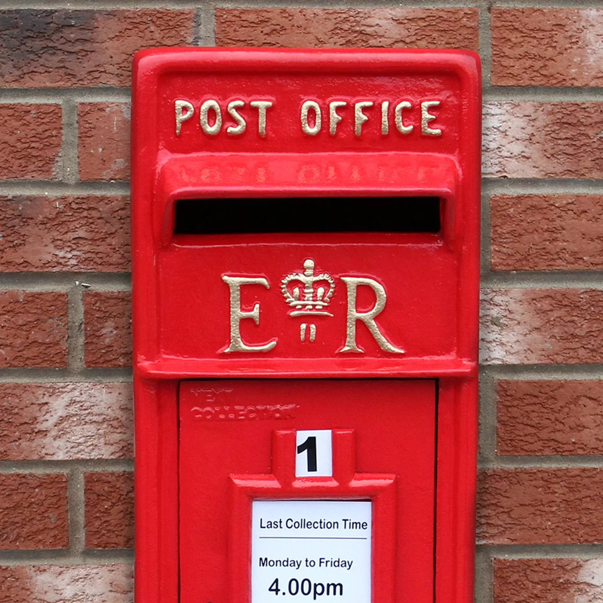 Bright red Royal Mail post box featuring gold lettering, a crown emblem, and a collection time notice against a brick wall