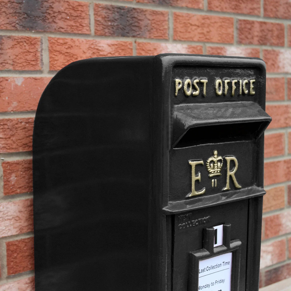 Black Royal Mail post box with gold lettering, featuring a curved top, textured metal surface, and collection time notice attached