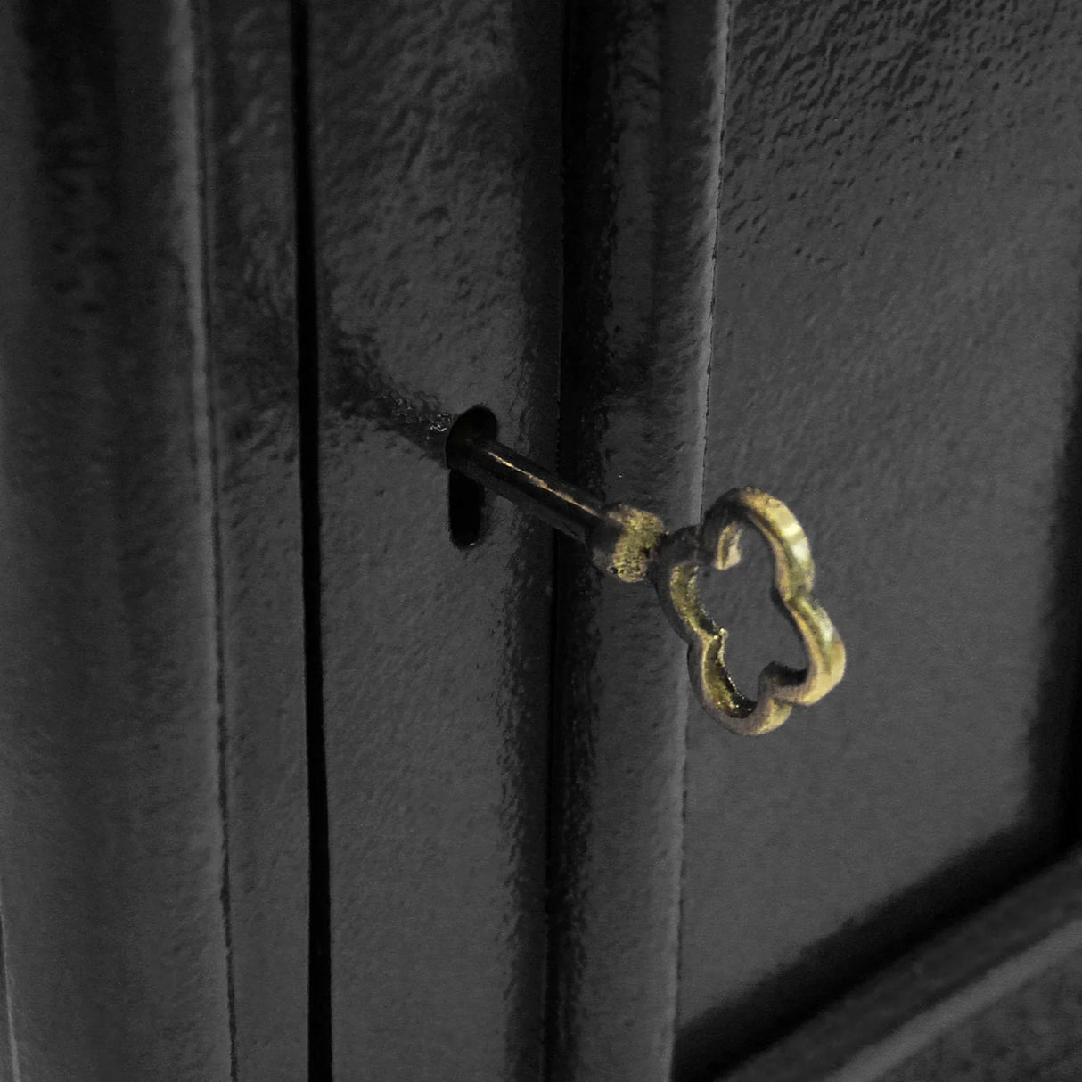 Black Royal Mail post box featuring a vintage keyhole with a decorative brass key, showcasing its sturdy metal texture and classic design