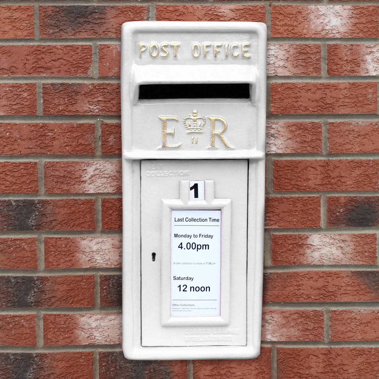 White Royal Mail post box mounted on a brick wall, featuring a crown emblem, collection times, and a classic design