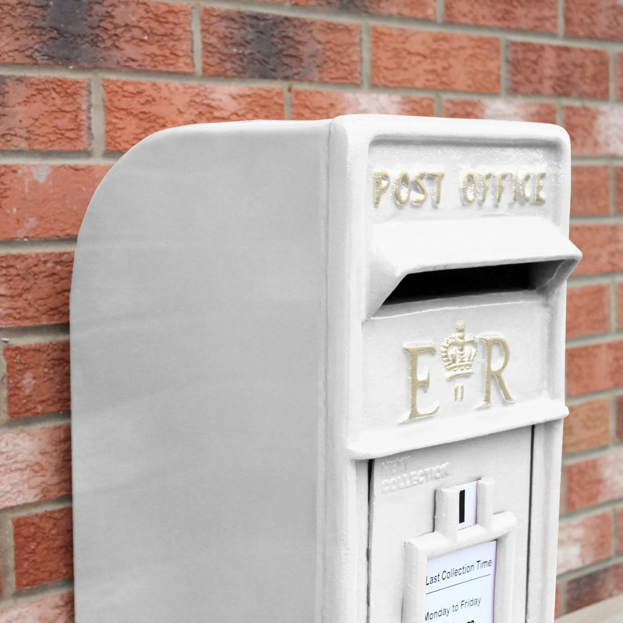 White Royal Mail post box with a smooth finish, featuring gold lettering and a collection slot, set against a brick wall