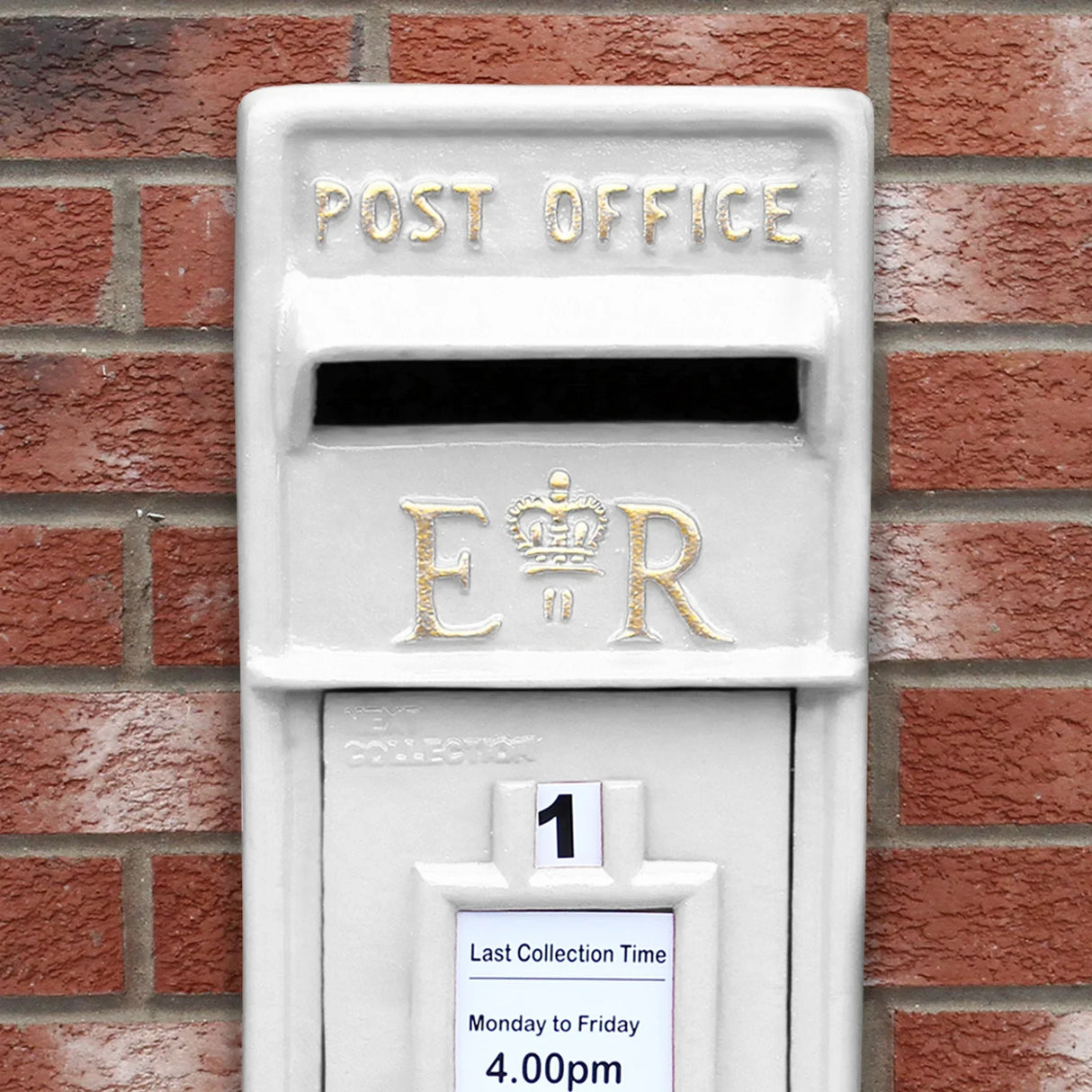 Elegant white Royal Mail post box featuring gold lettering, collection time notice, and classic design against a brick wall