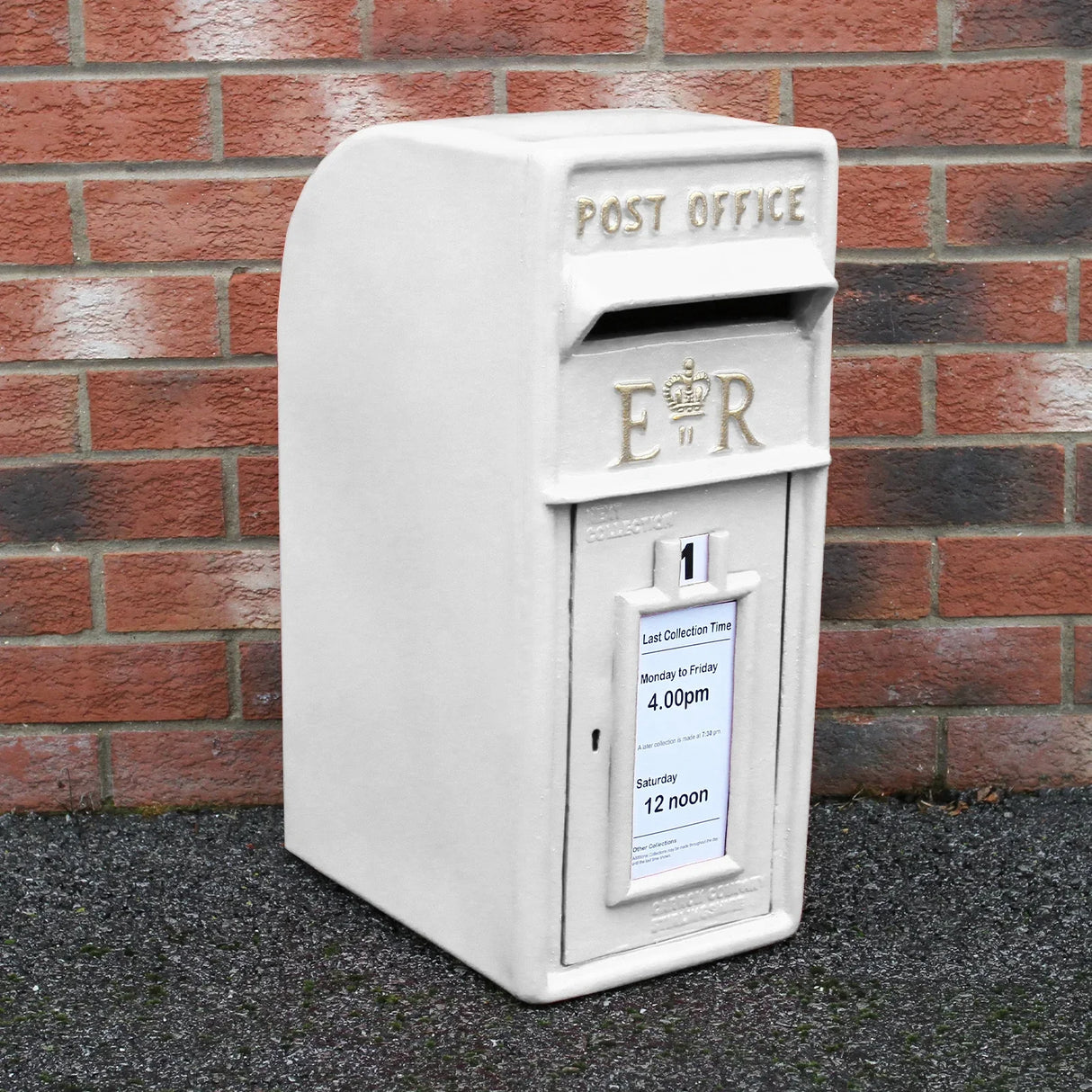 White Royal Mail post box with stand, featuring a textured surface, engraved lettering, and collection time notice against a brick wall