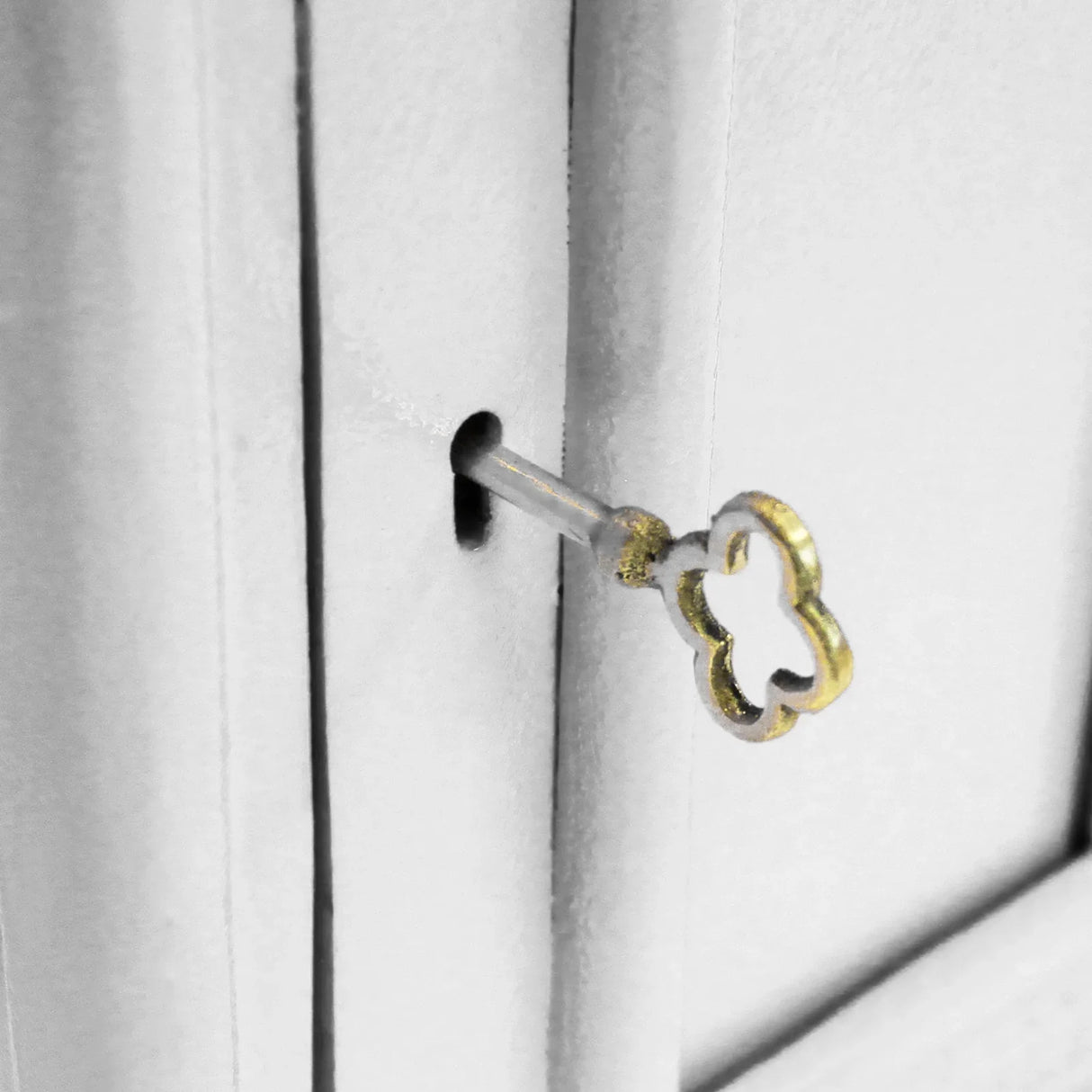 Detailed close-up of a vintage white Royal Mail post box keyhole with a decorative gold key inserted, showcasing intricate design elements