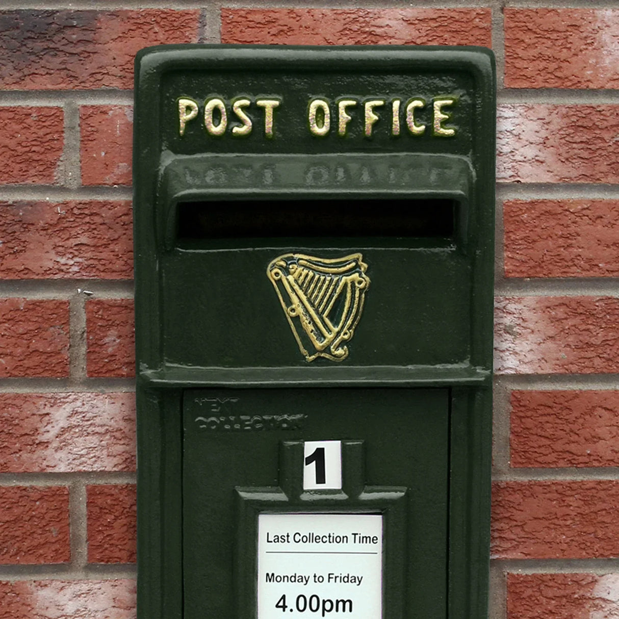 Green Irish post box with gold lettering, featuring a harp design, mounted on a brick wall, showcasing collection times and stand