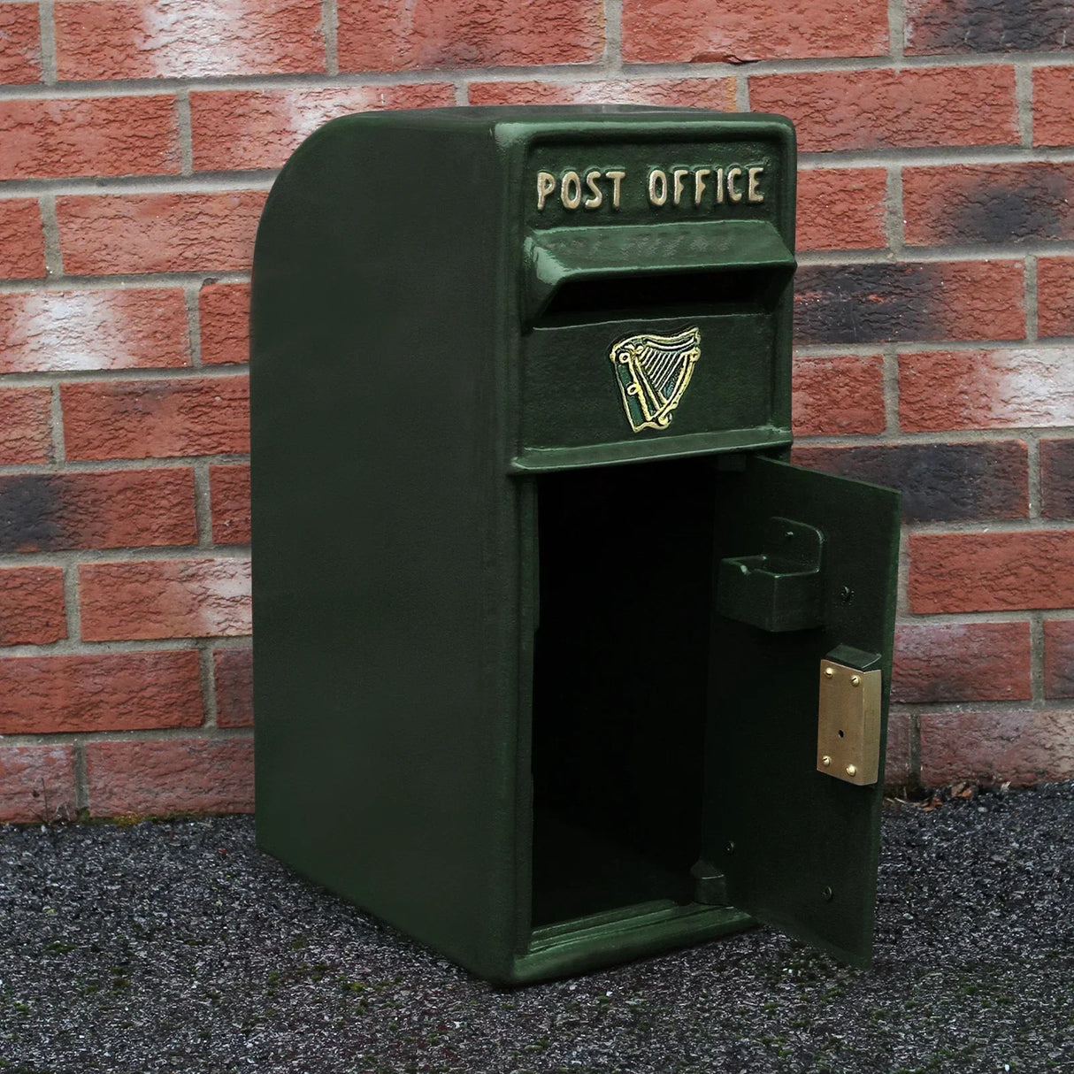 Green Irish post box with a gold harp emblem, featuring a classic design and a sturdy stand, set against a brick wall background