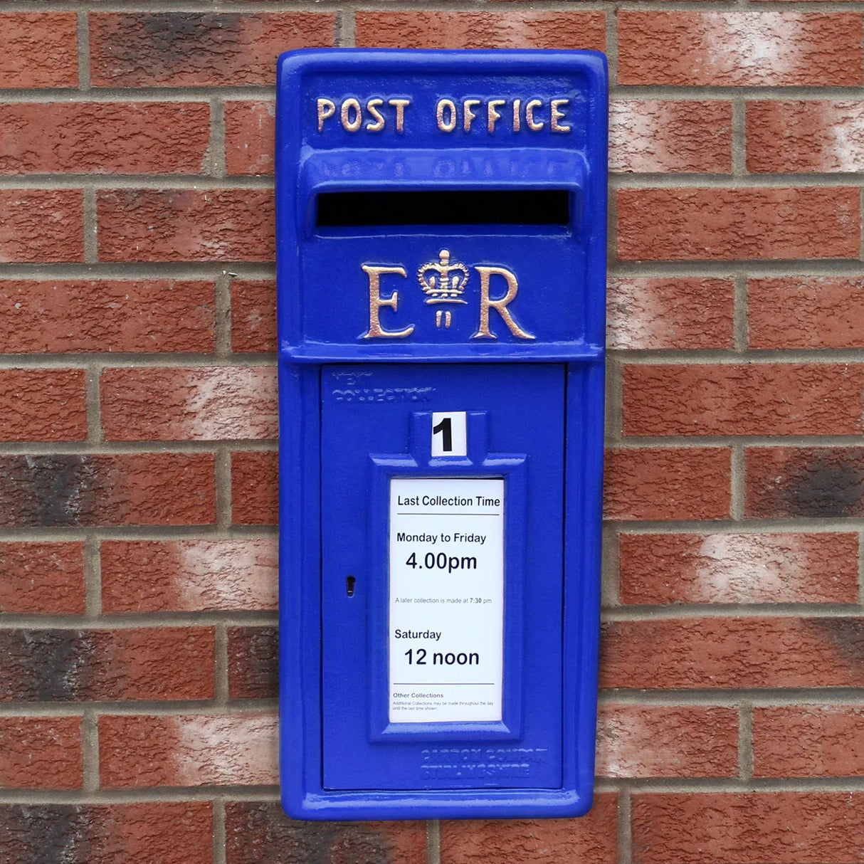 Bright blue Scottish post box with gold lettering, mounted on a brick wall, featuring collection times and a royal emblem