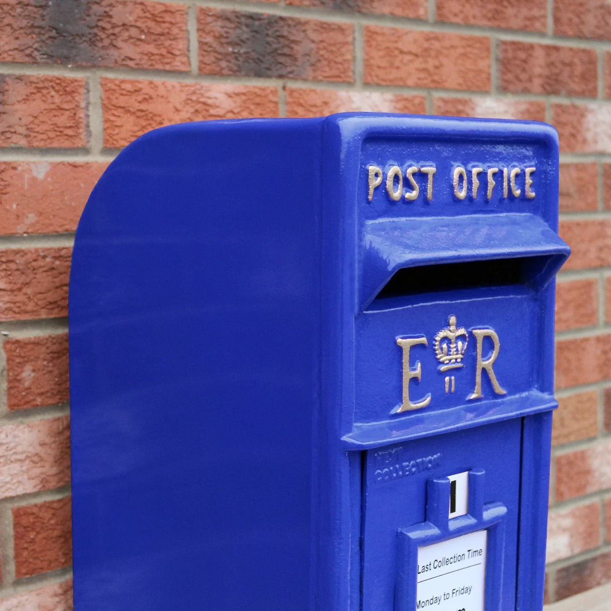 Bright blue Scottish post box with gold lettering, featuring a crown emblem and a collection slot, mounted on a brick wall