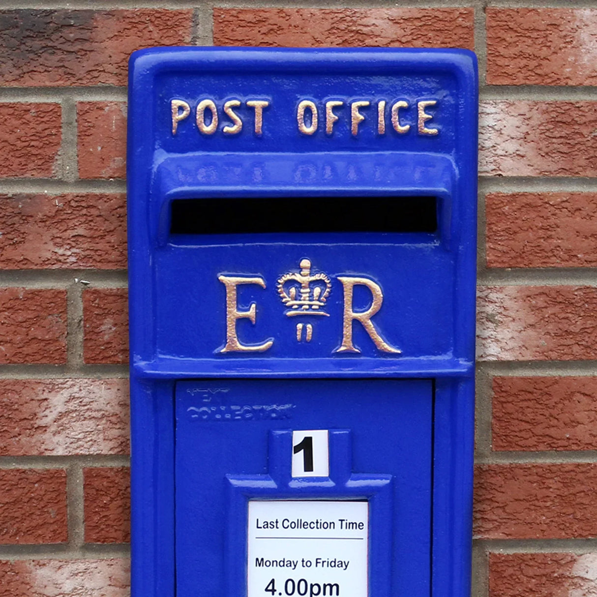 Bright blue Scottish post box featuring gold lettering, a crown emblem, and a collection time notice on a brick wall