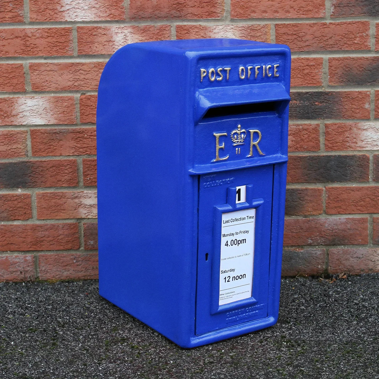 Bright blue Scottish post box with a royal emblem, featuring a collection time notice, set against a brick wall background