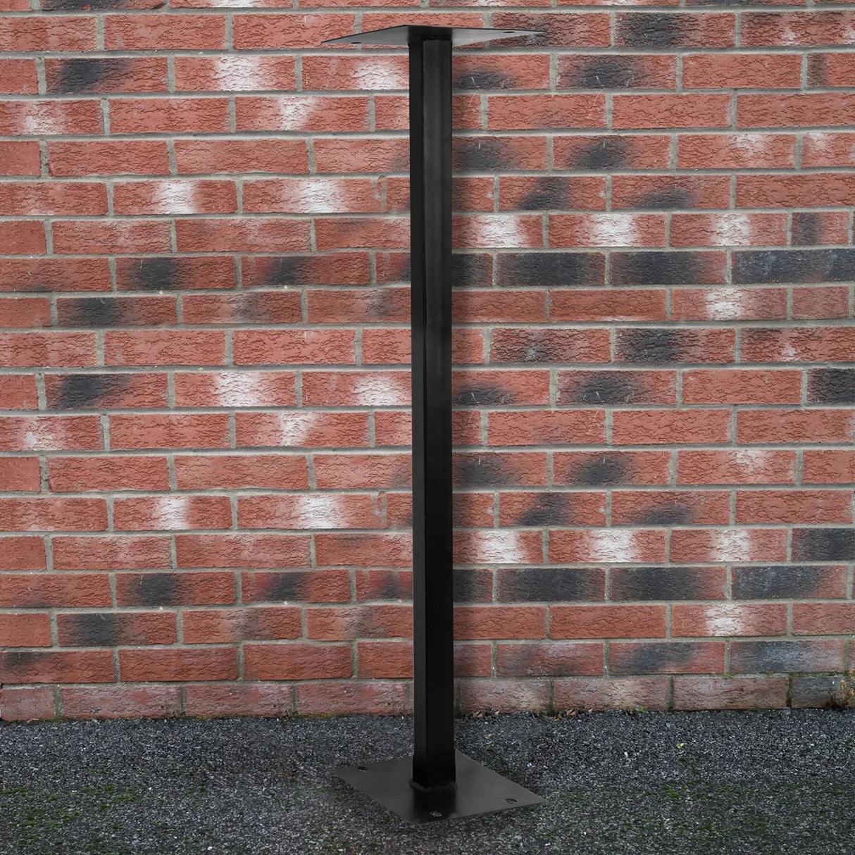 Black metal stand for a white Royal Mail post box, featuring a sturdy base and tall, sleek design against a brick wall backdrop