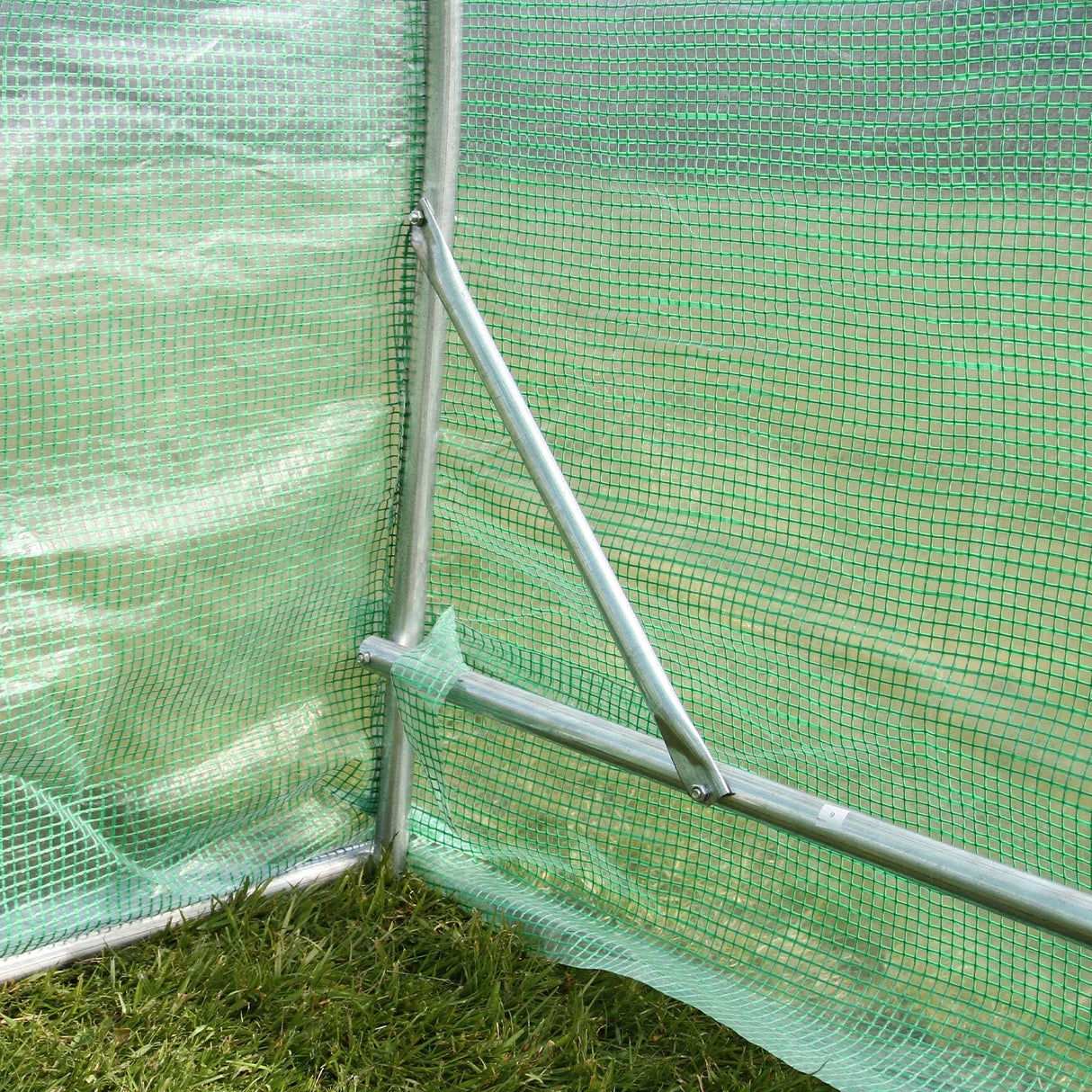 Close-up of the Polytunnel 19mm frame showing green mesh covering, sturdy metal supports, and grass beneath for stability