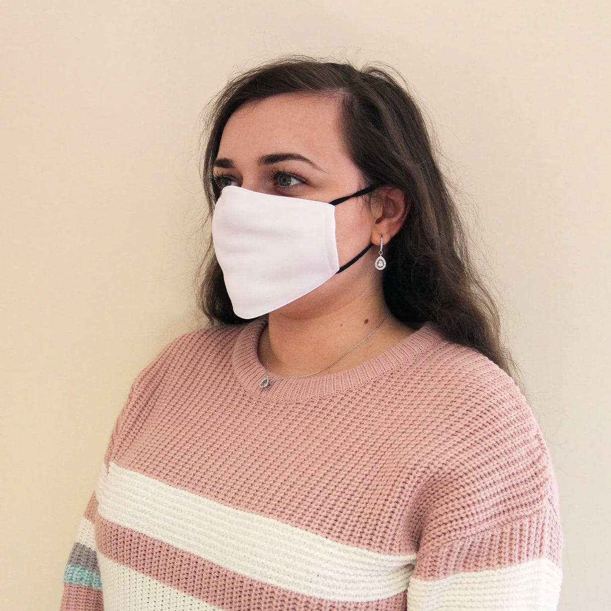 White fabric face mask worn by a woman with long hair, featuring a snug fit and adjustable ear loops, against a neutral...
