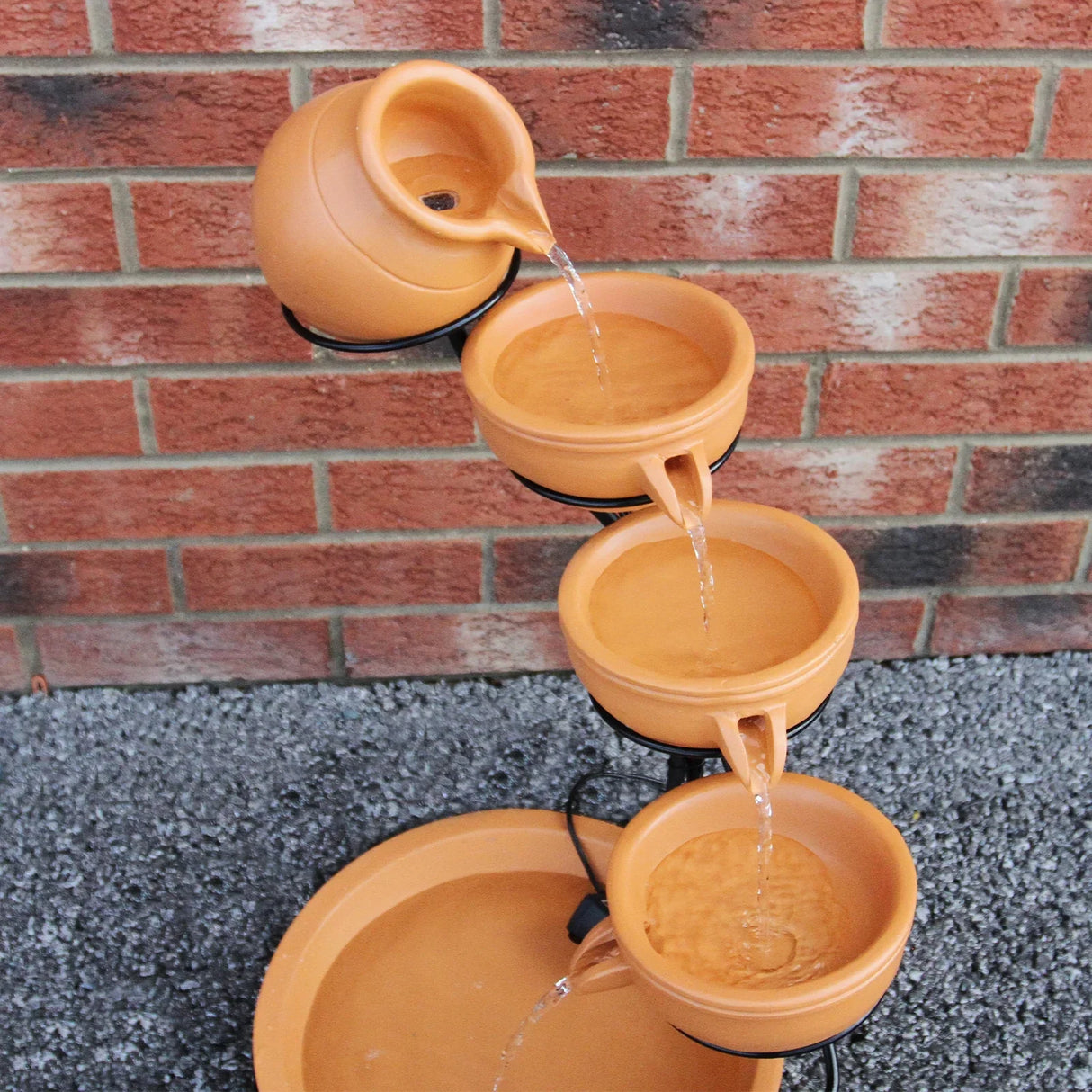 Terracotta 4 tier spilling bowls water feature with flowing water, earthy orange color, and smooth, rounded shapes against a brick backdrop