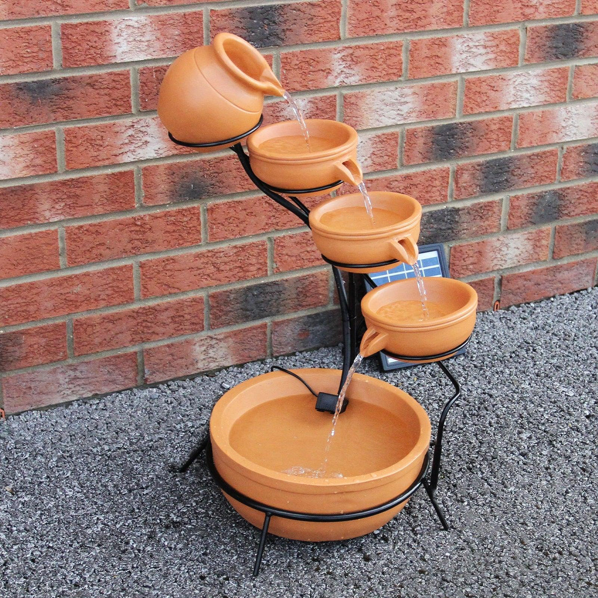 Terracotta 4 tier spilling bowls water feature with flowing water, set on a black metal frame against a brick wall background