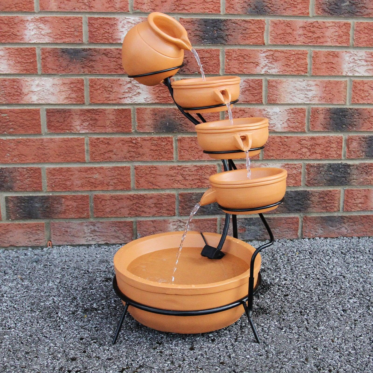 Terracotta 4 tier spilling bowls water feature with flowing water, set on a black metal frame against a brick wall background