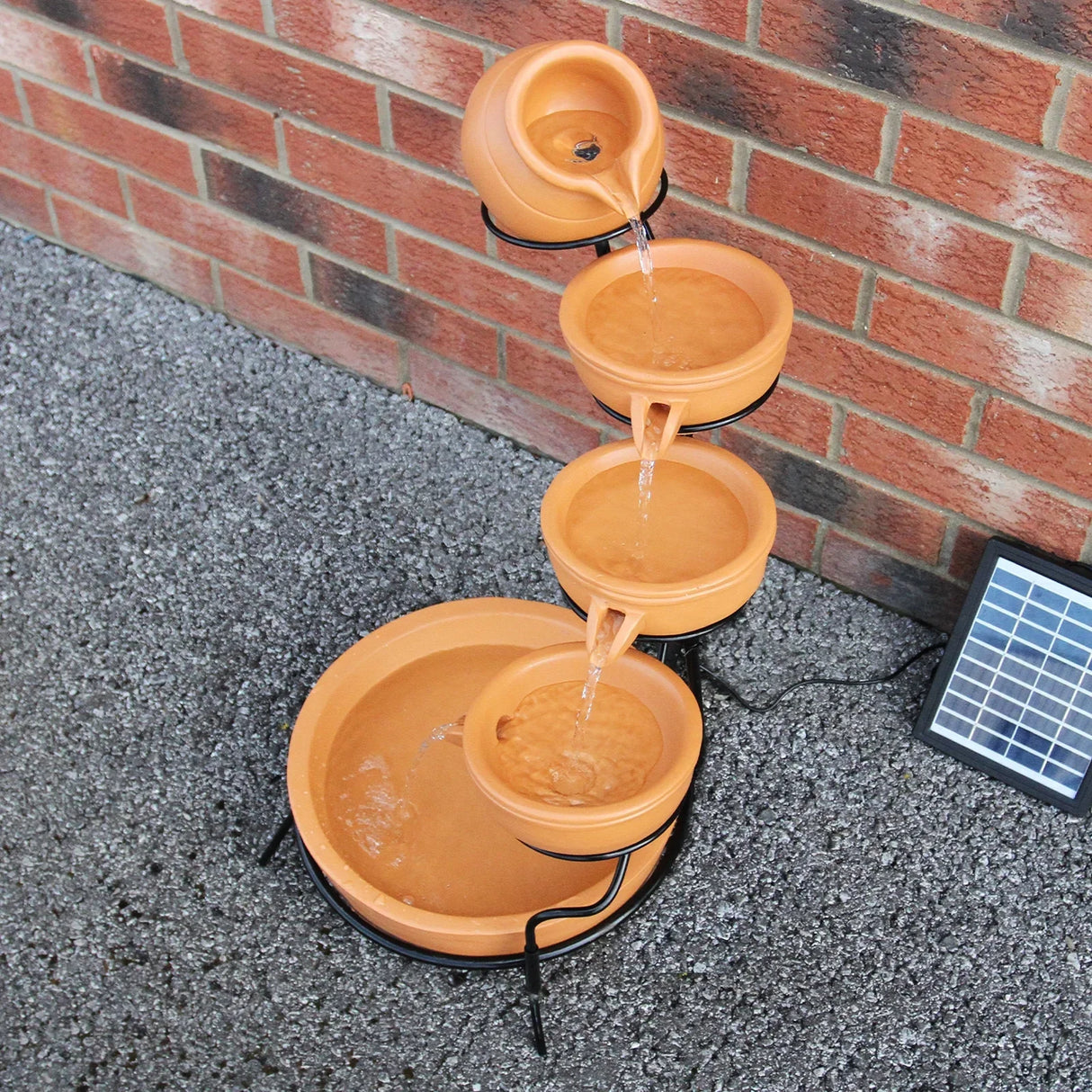 Terracotta 4 tier water feature with cascading bowls, earthy orange color, and a sleek black metal stand, ideal for gardens