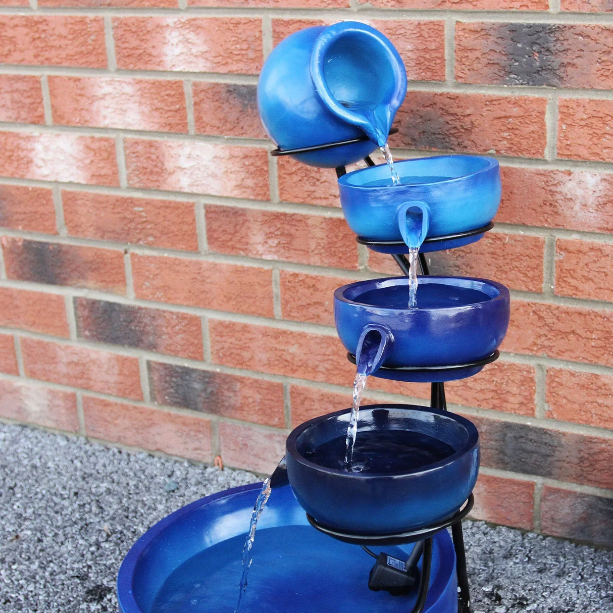 Blue 4 tier spilling bowls water feature with cascading water, textured ceramic bowls in varying shades of blue against a brick wall