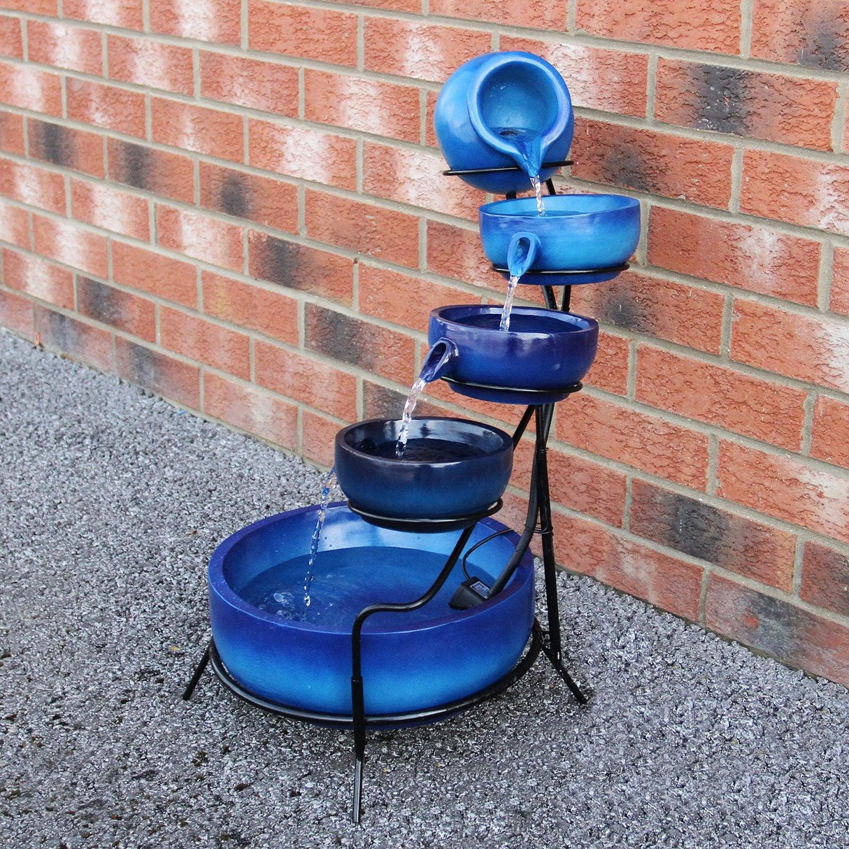Blue 4 tier spilling bowls water feature with cascading water, glossy ceramic finish, and sturdy black metal frame against a brick wall