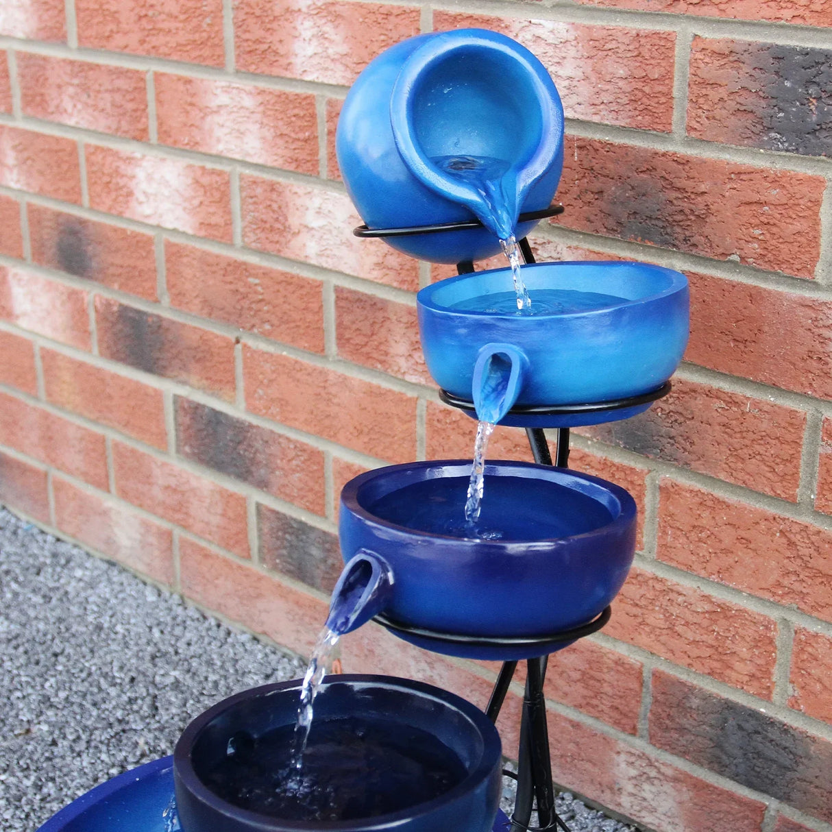 Four-tier water feature with blue ceramic bowls cascading water, set against a textured brick wall, enhancing outdoor decor