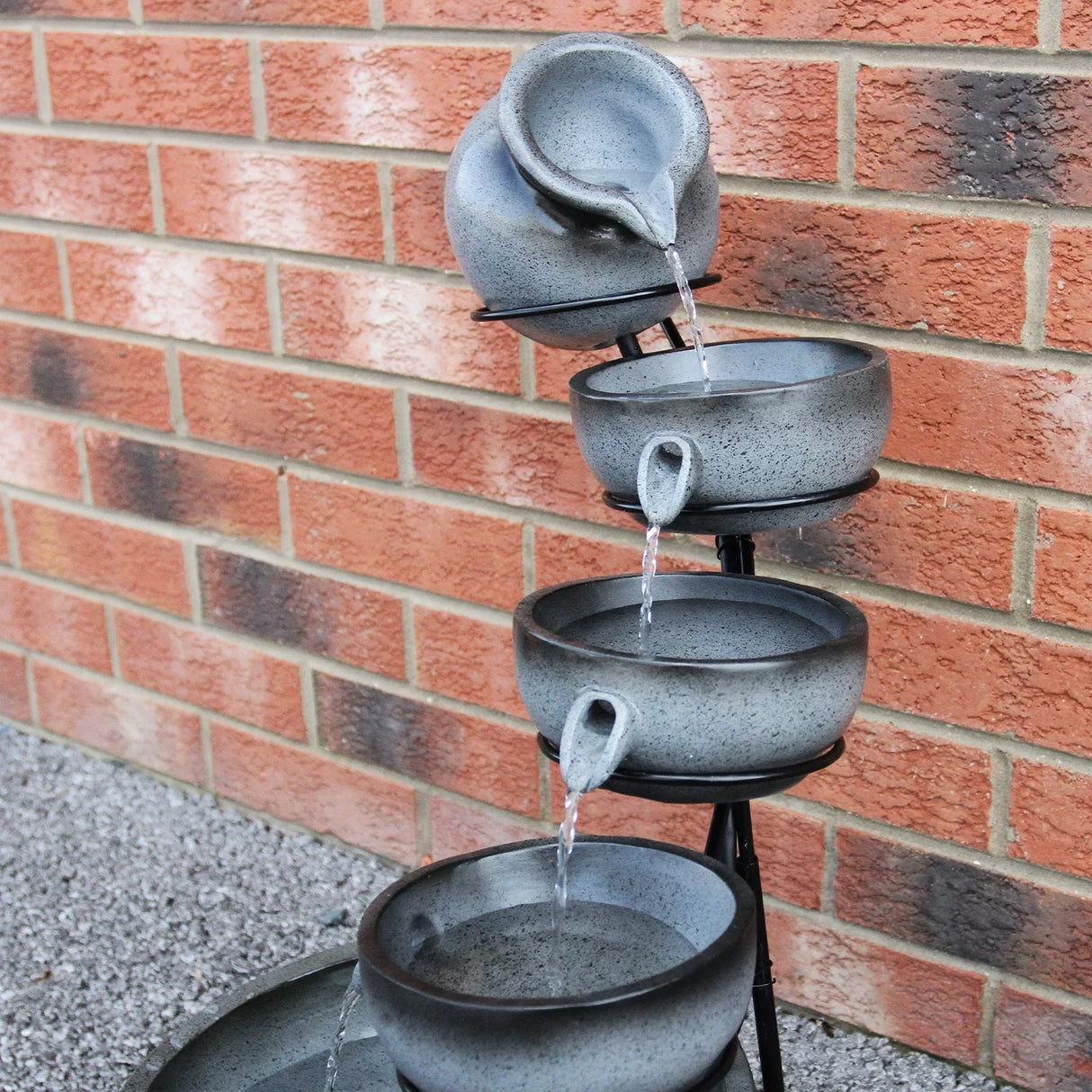 Grey 4 tier spilling bowls water feature with textured ceramic bowls cascading water, set against a brick wall background