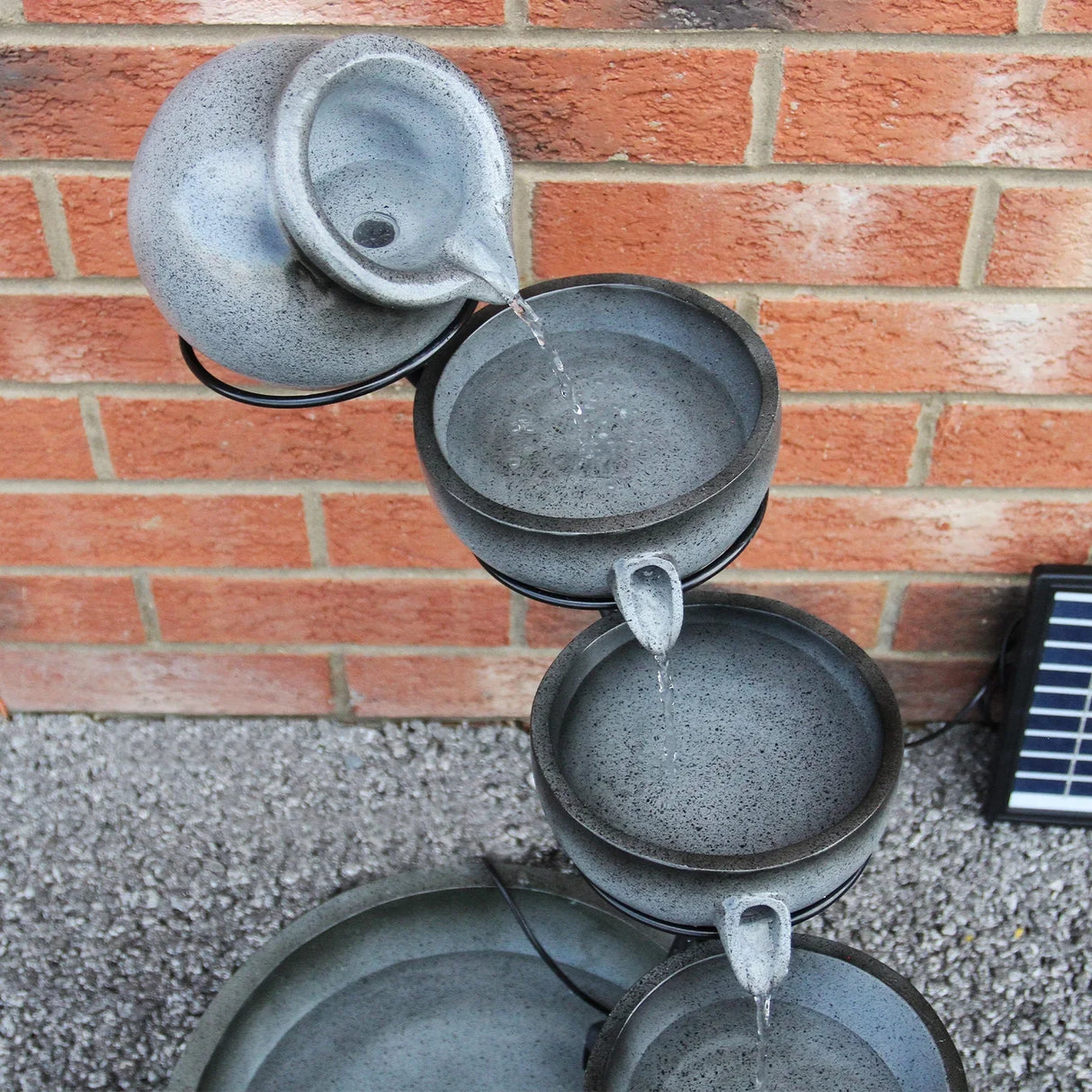 Grey 4 tier spilling bowls water feature with textured ceramic bowls, cascading water, and a rustic design against a brick wall