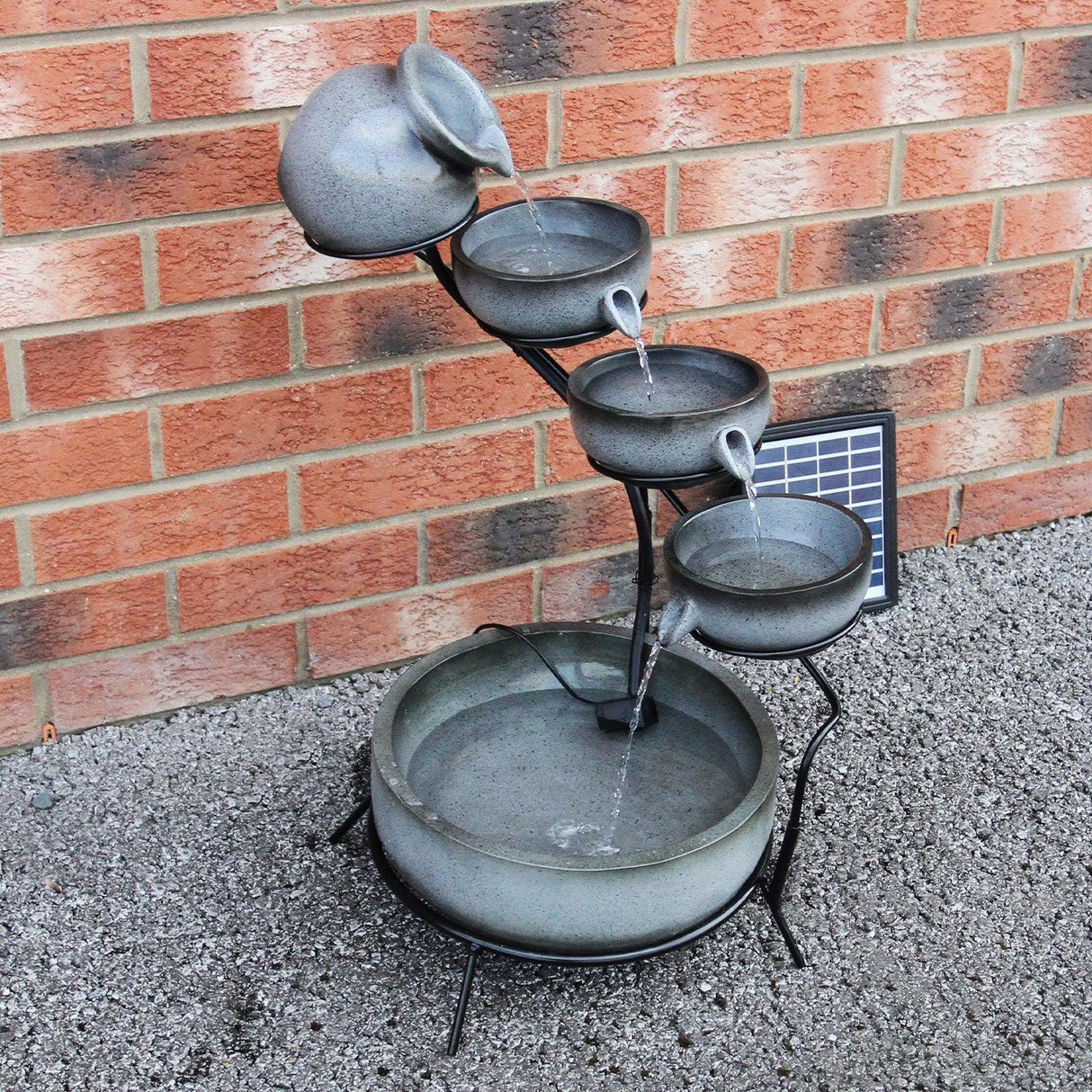 Grey 4 tier spilling bowls water feature with a sleek design, cascading water from bowls into a round base, set against a brick wall