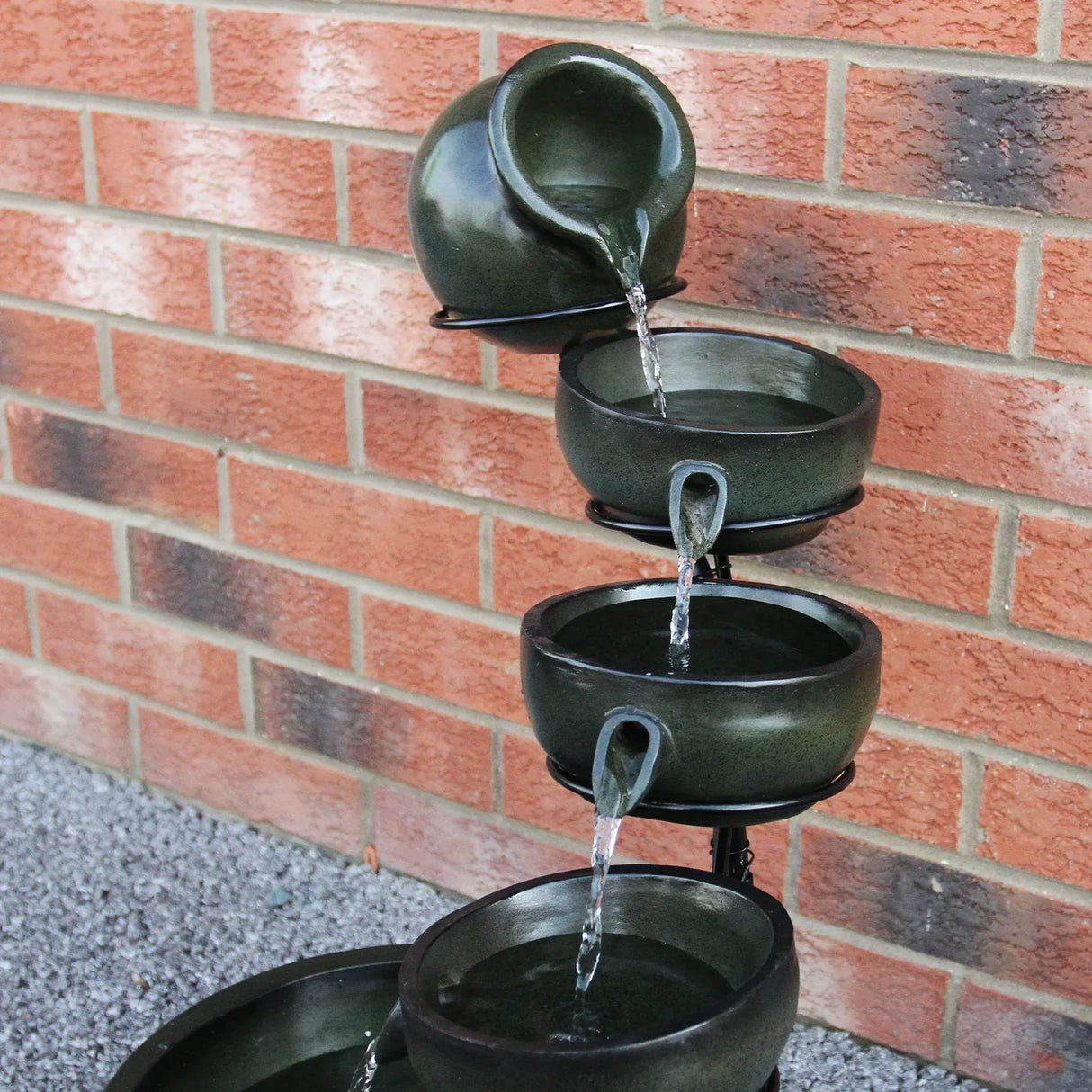Green 4 tier spilling bowls water feature with a textured finish, cascading water from each bowl against a brick wall backdrop
