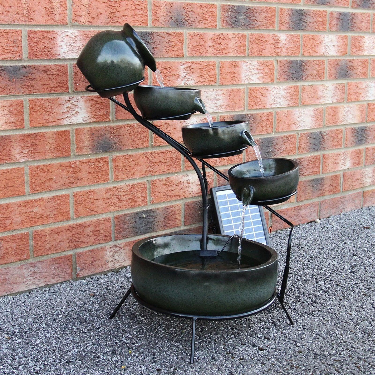Green 4 tier spilling bowls water feature with a sleek black frame, cascading water, and solar panel, set against a brick wall