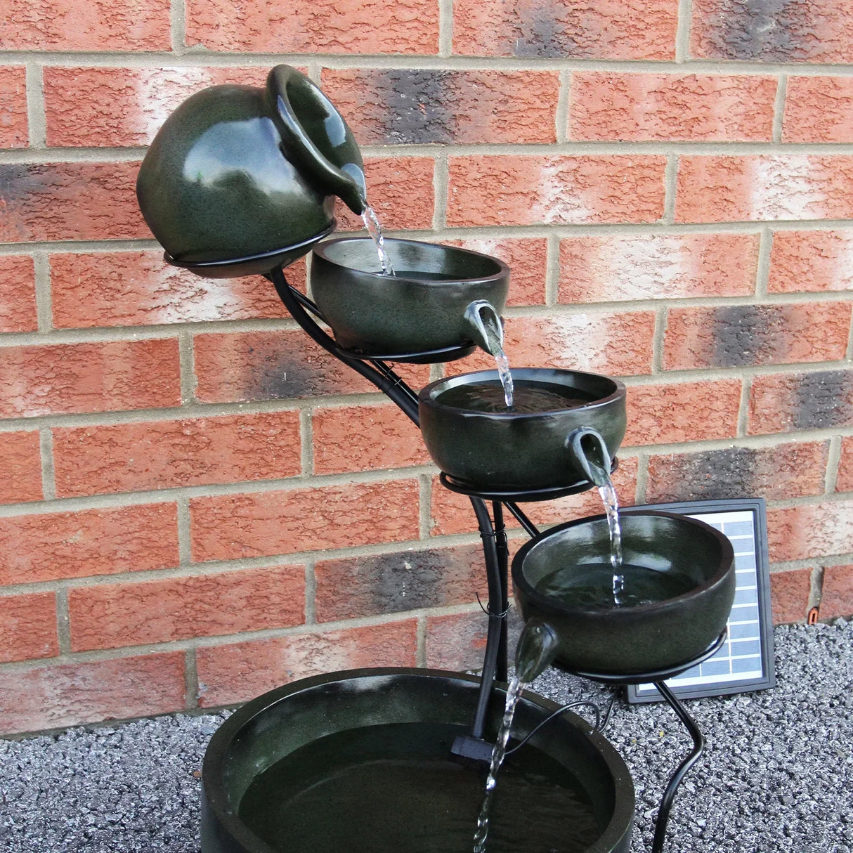 Green 4 tier spilling bowls water feature with cascading water, ceramic texture, and a sleek black metal stand against a brick wall
