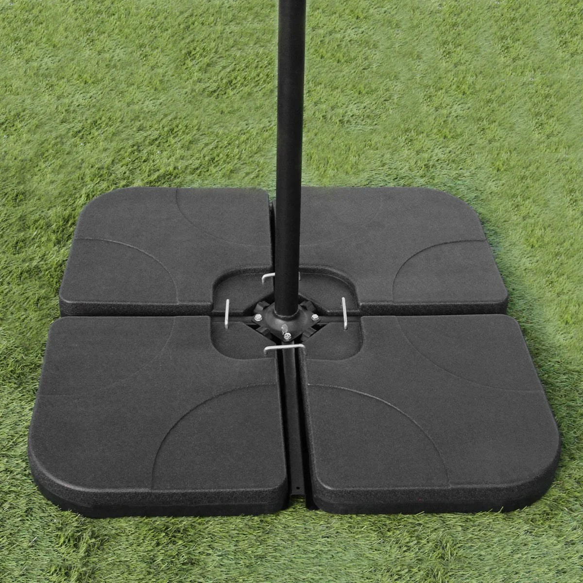 Cantilever parasol base with a sturdy black design, featuring four interlocking sections, placed on green grass for stability