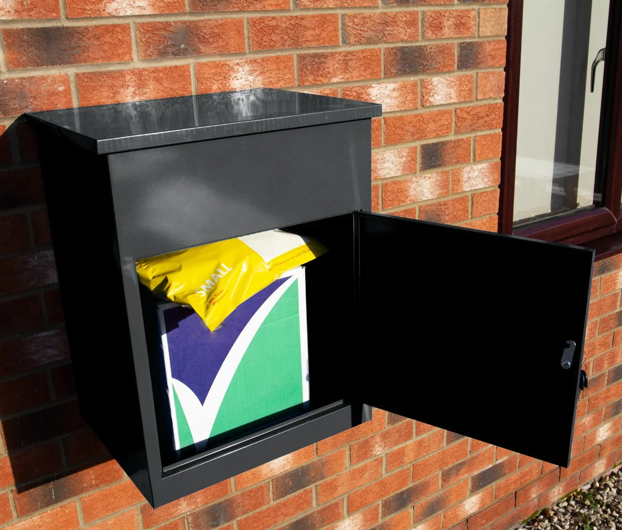 Sleek black parcel post box mounted on a brick wall, featuring a secure opening with a colorful package inside for deliveries