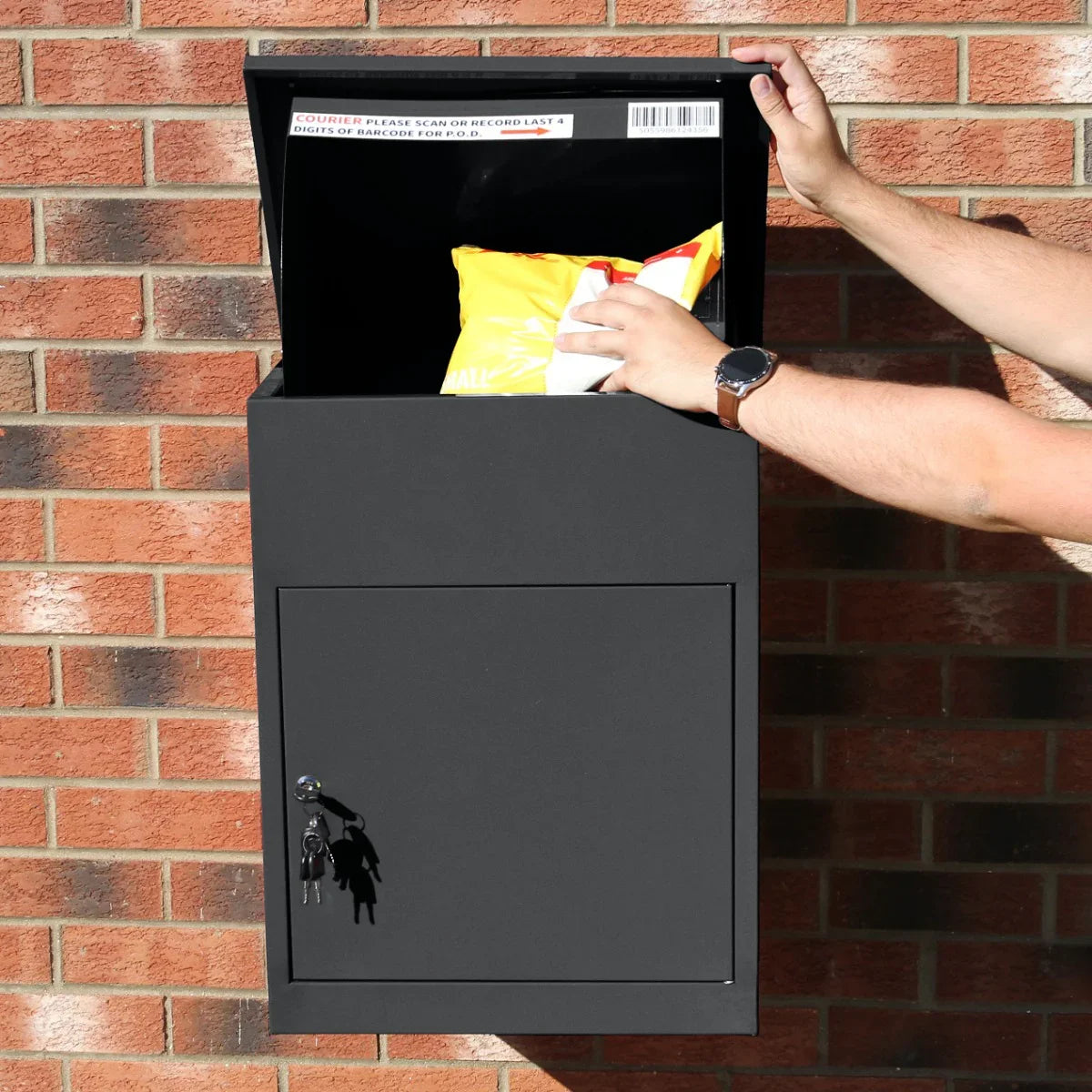 Sleek black parcel post box with a secure locking door, open to reveal a package inside, set against a brick wall backdrop
