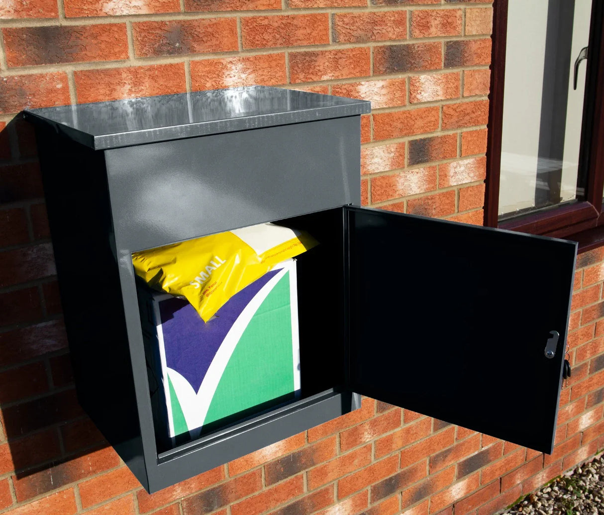 Grey parcel post box mounted on a brick wall, featuring a secure opening with a colorful package inside, ideal for safe deliveries