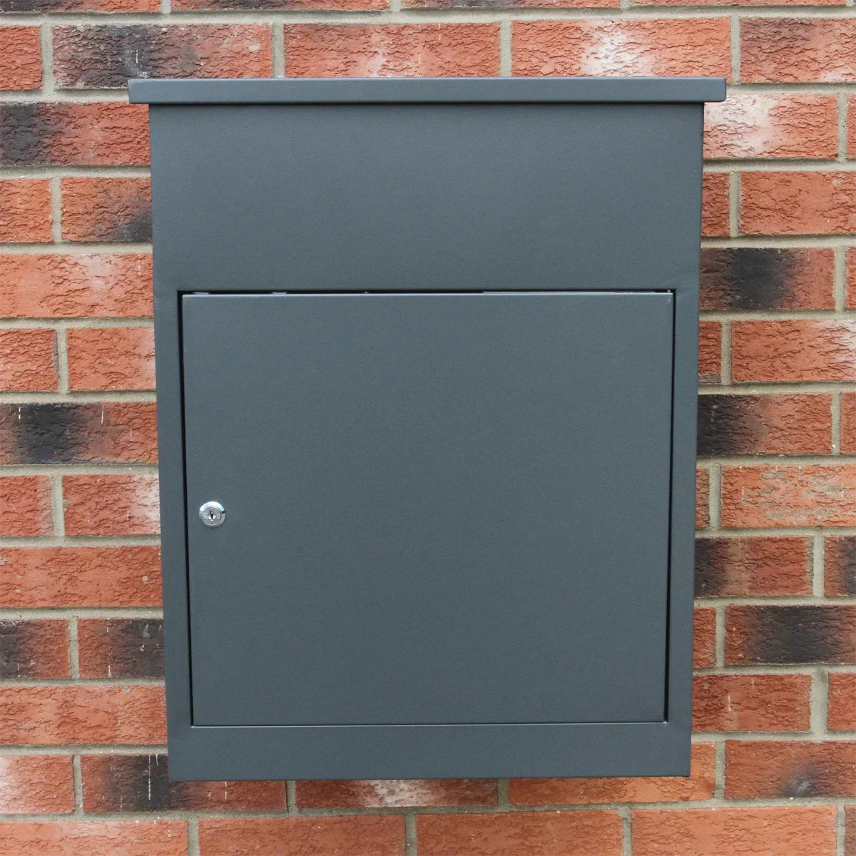 Grey parcel post box with a sleek design, featuring a secure front door and a smooth matte finish against a brick wall backdrop