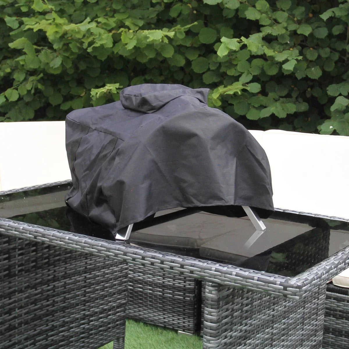 Black protective cover for an outdoor tabletop pizza oven, fitted over a sleek, modern design resting on a glass-top table
