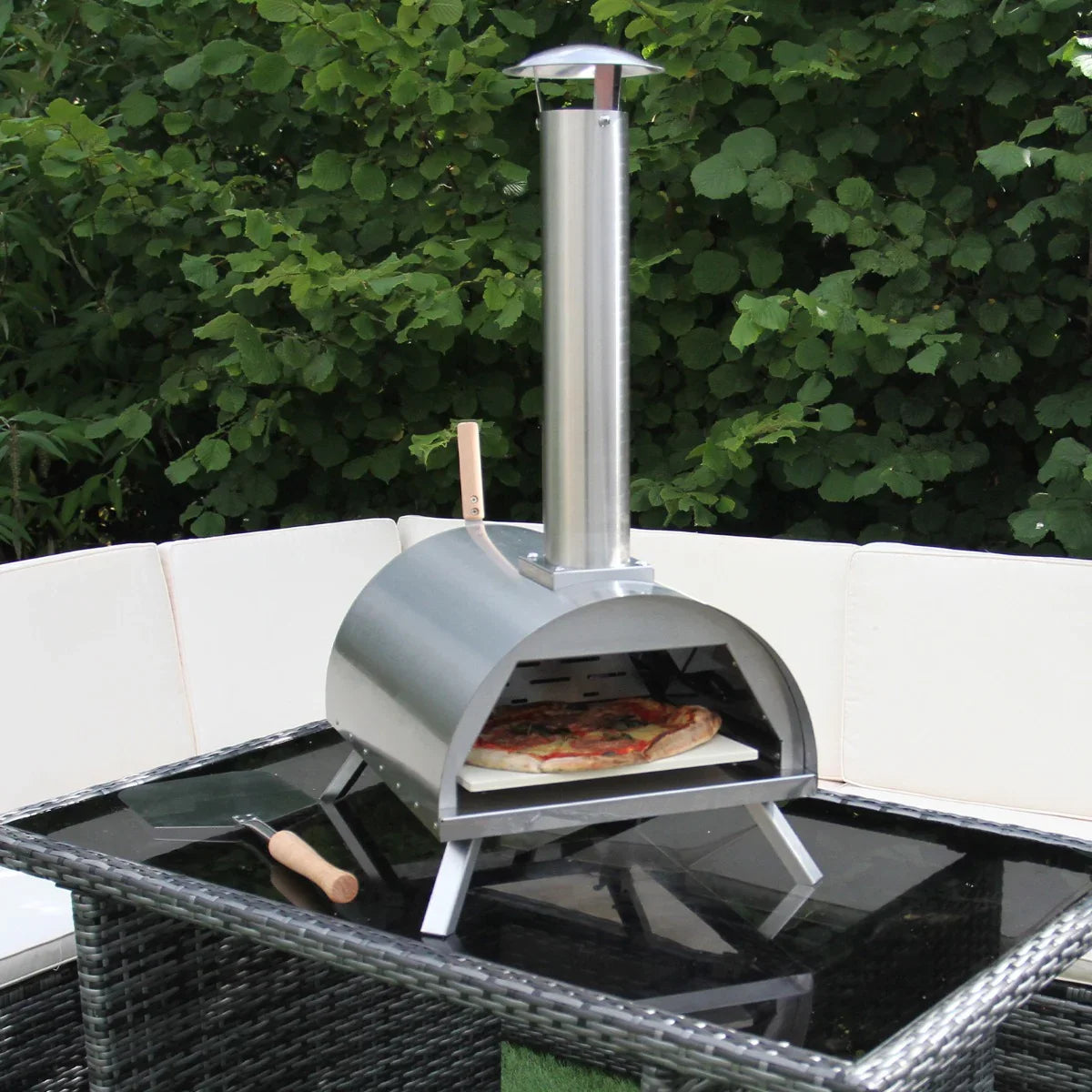 Outdoor table top pizza oven with a sleek stainless steel design, chimney, and a freshly baked pizza on a black glass table