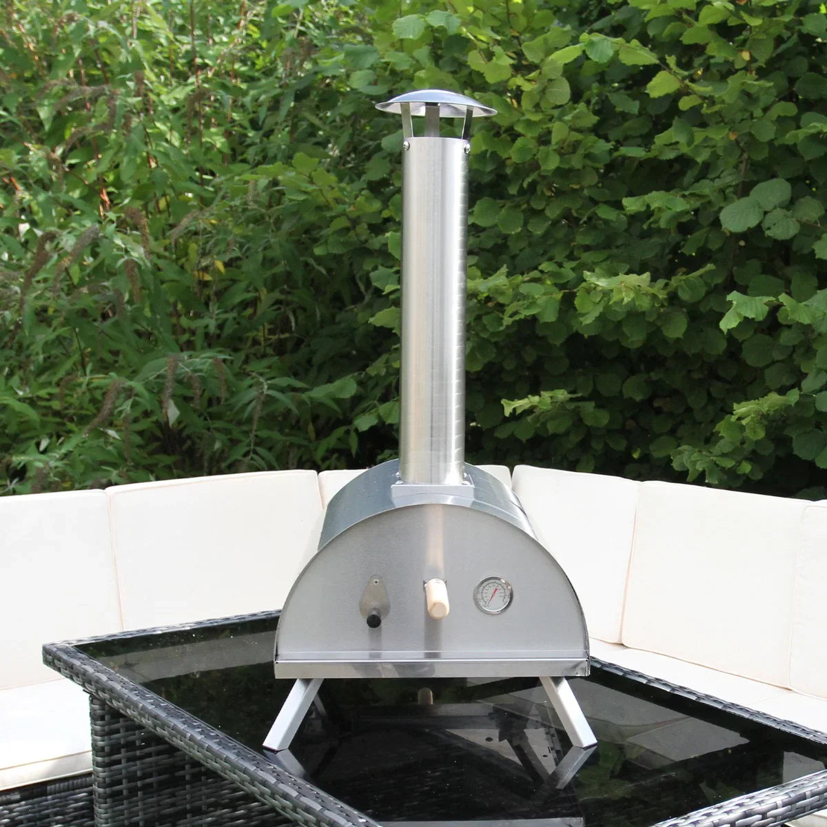 Outdoor table top pizza oven with a sleek stainless steel design, chimney, and temperature gauge, set on a black glass table