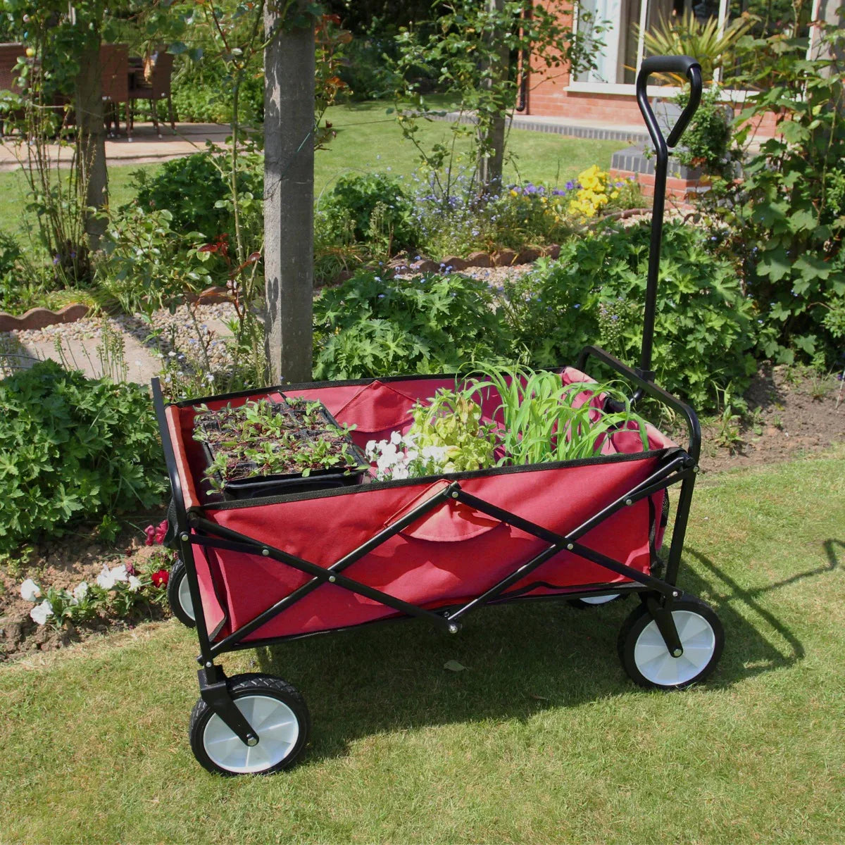 Foldable garden cart in vibrant red with a sturdy black frame, filled with flowers and plants, set against a lush garden backdrop