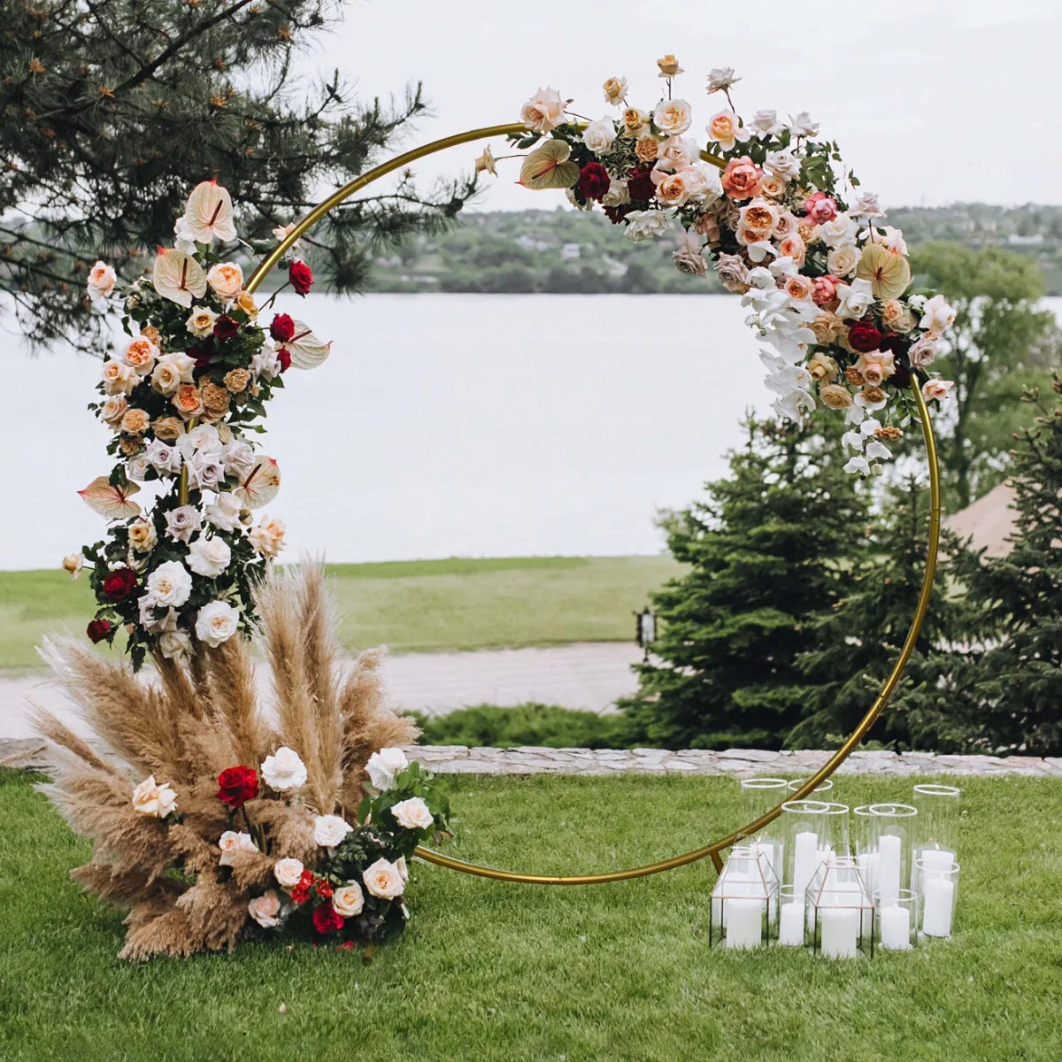 Elegant gold wedding moongate adorned with vibrant flowers, pampas grass, and candles, set against a scenic outdoor backdrop