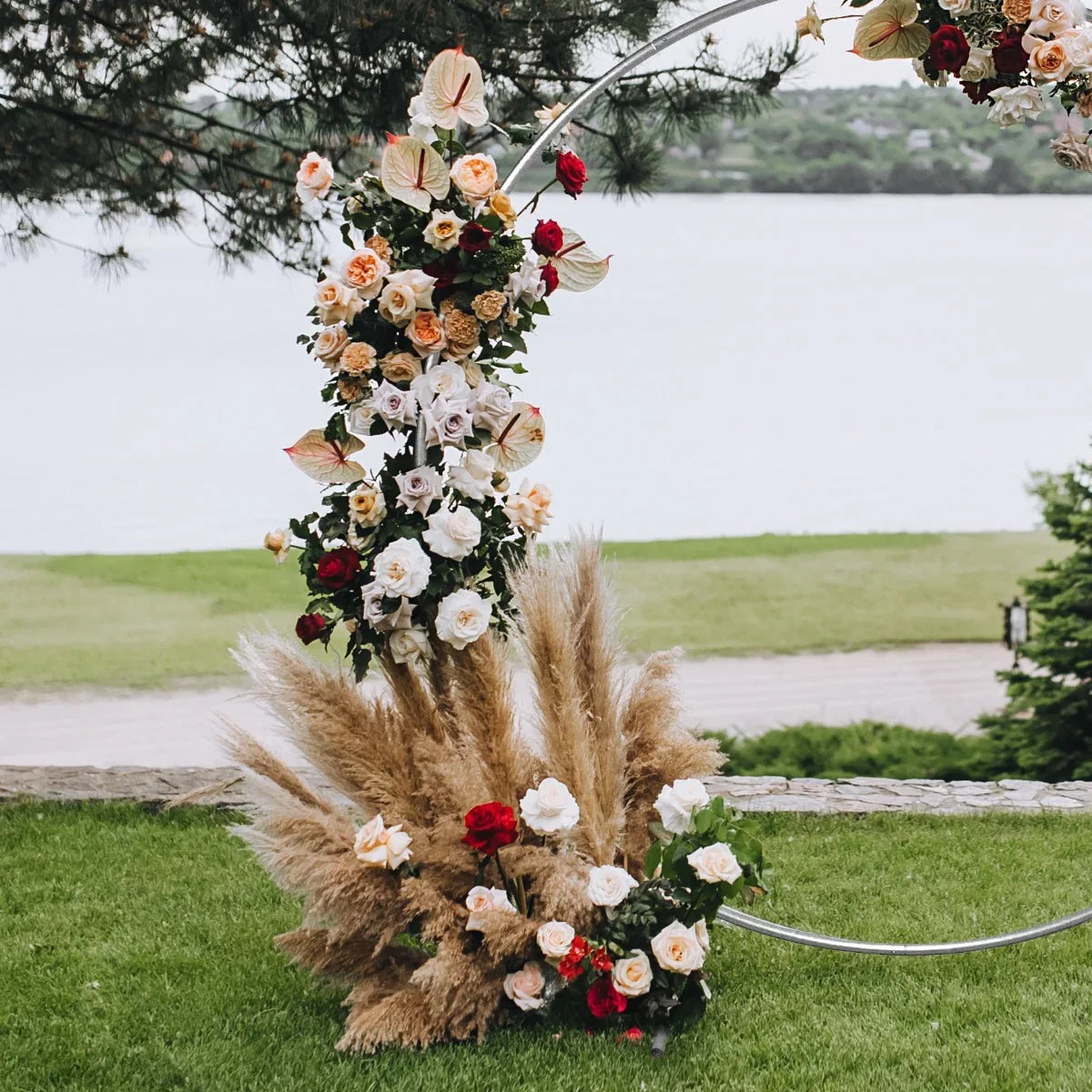 Elegant silver wedding moongate adorned with lush roses and pampas grass, set against a serene waterfront backdrop