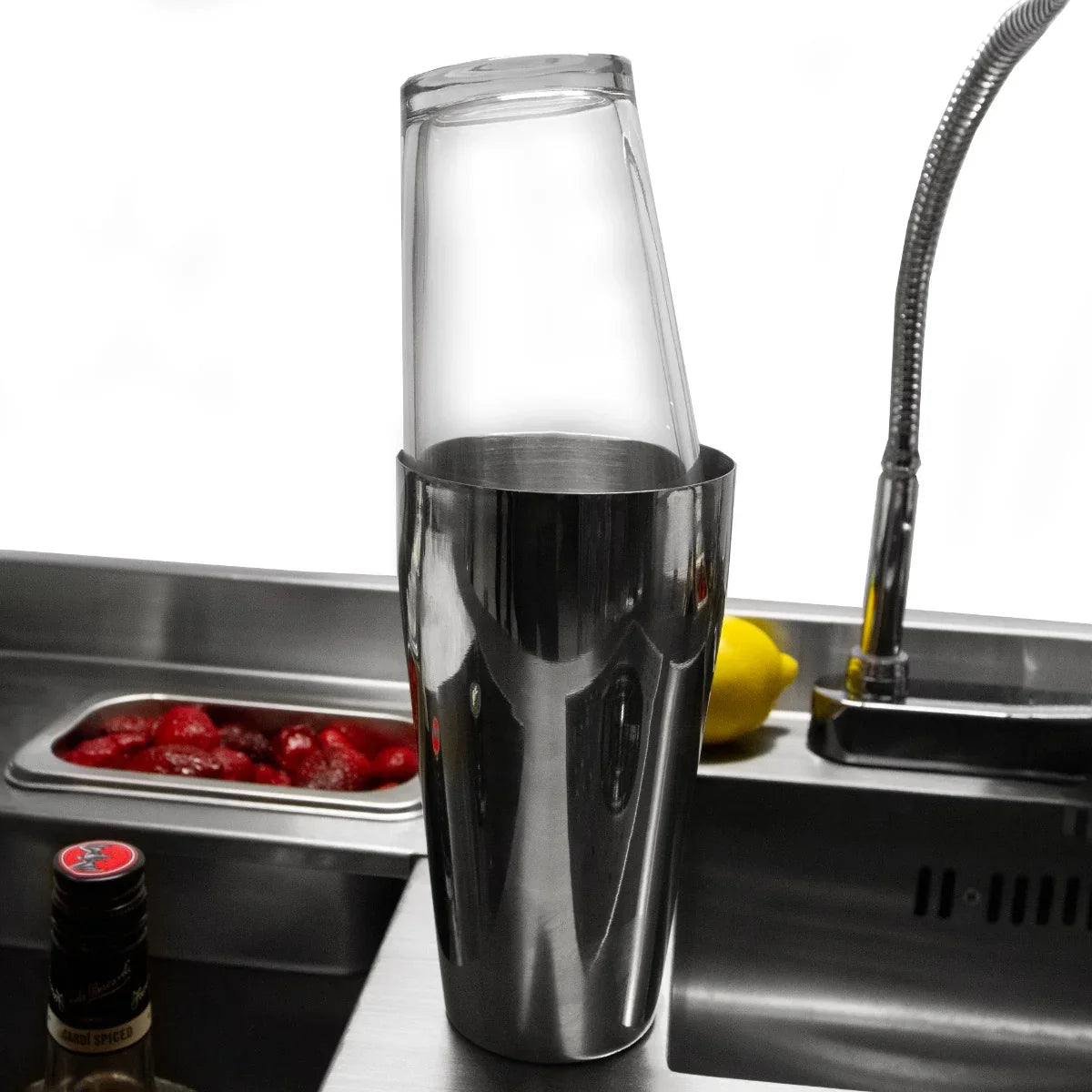 Stainless steel cocktail shaker with a clear glass top, resting in a sleek bar station, surrounded by fresh ingredients and tools