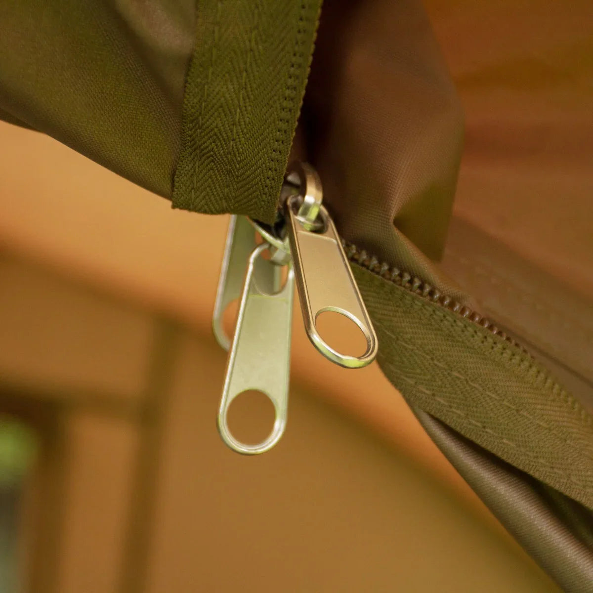 Close-up of a durable zipper on a green fishing bivvy, showcasing high-quality metal pulls and sturdy fabric for outdoor use