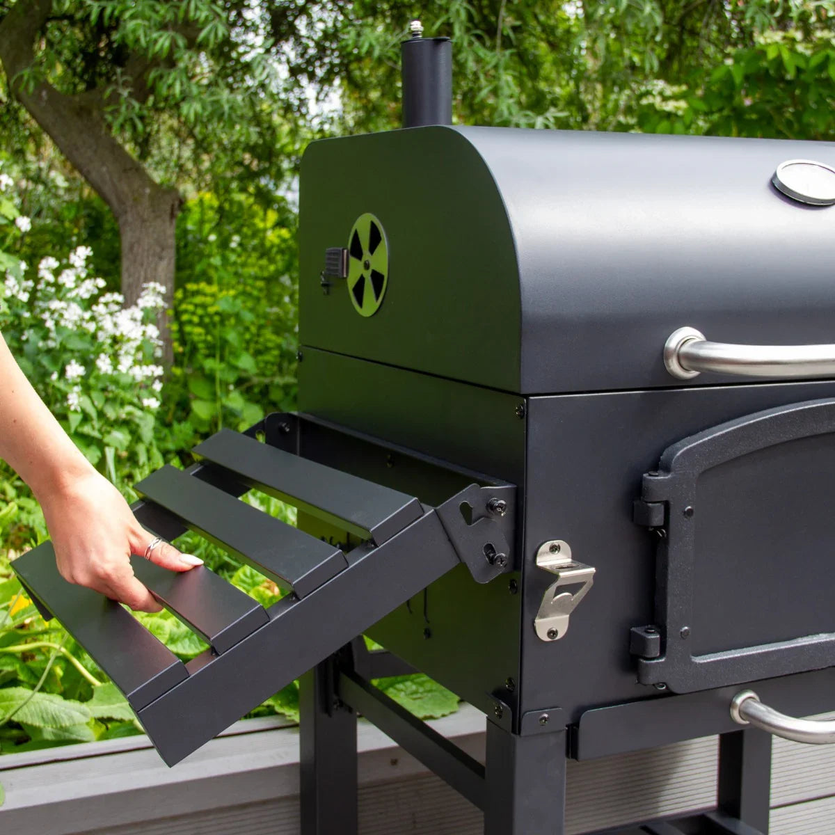 XL BBQ smoker with a sleek black finish, featuring a side shelf and sturdy construction, set against a lush garden backdrop