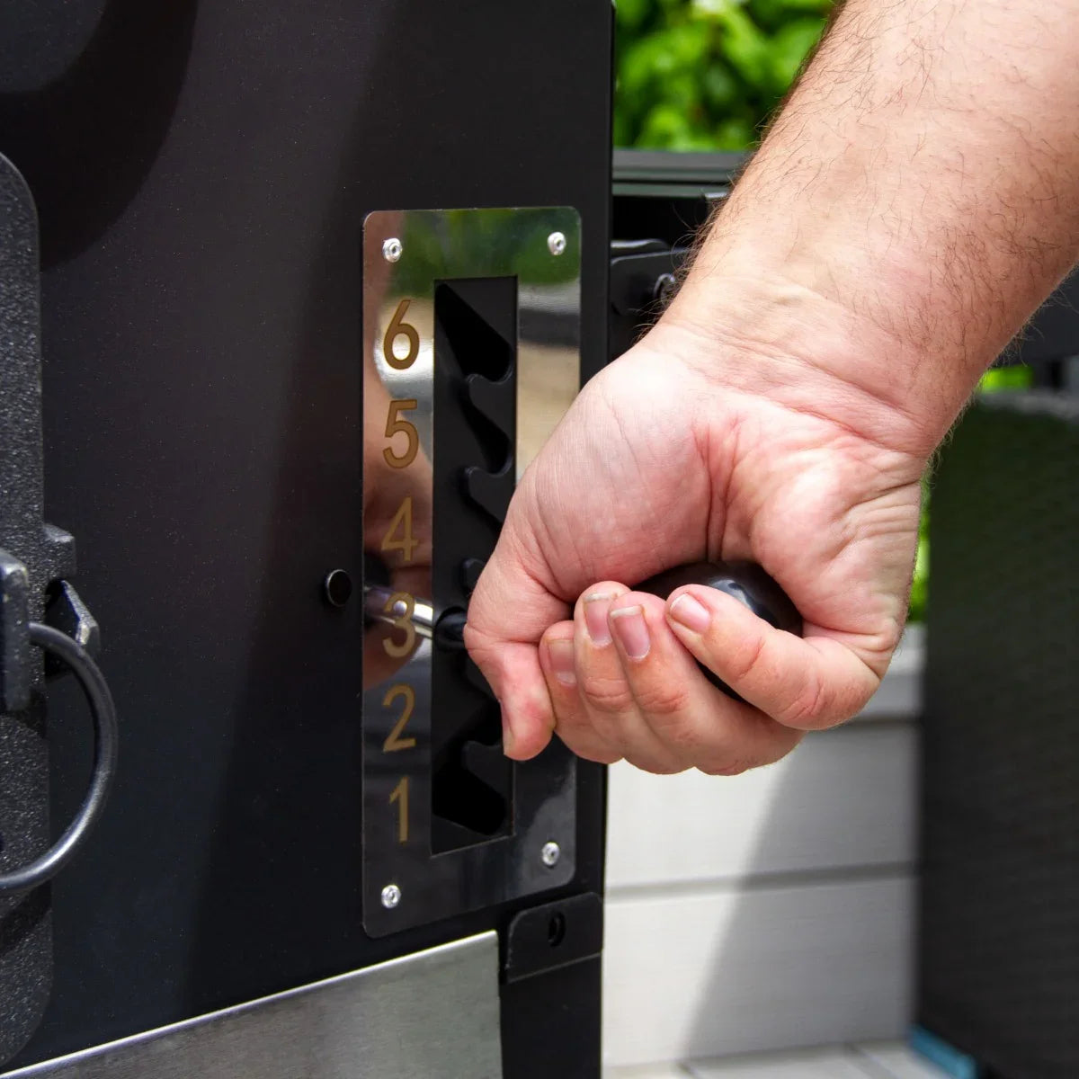 Hand adjusting the temperature control dial on the XXL BBQ Smoker, featuring a sleek black finish and stainless steel accents