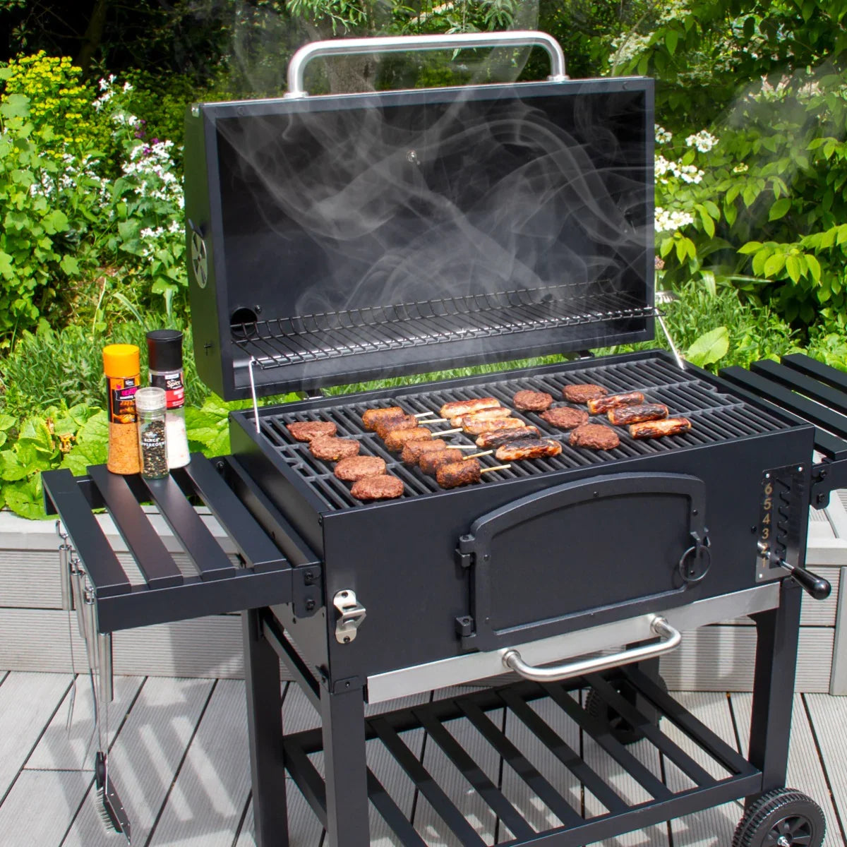 XXL BBQ smoker with a black finish, open lid revealing sizzling meats, smoke rising, and spice jars on the side table