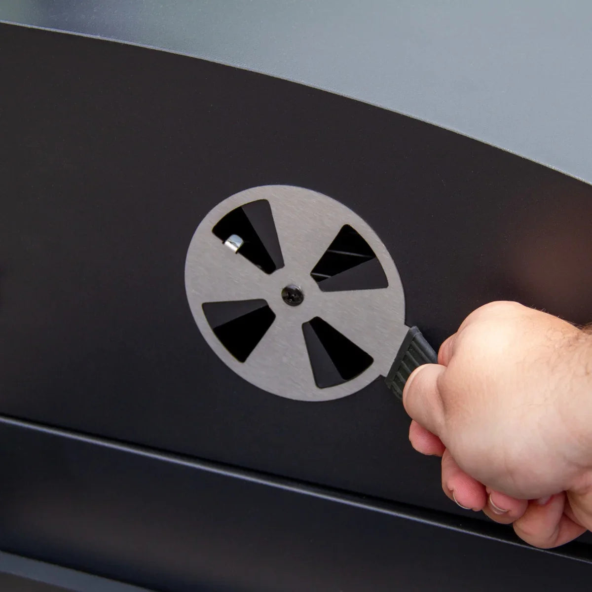 Hand adjusting the air vent on the XXL BBQ smoker, featuring a sleek black finish and sturdy metal construction for optimal airflow